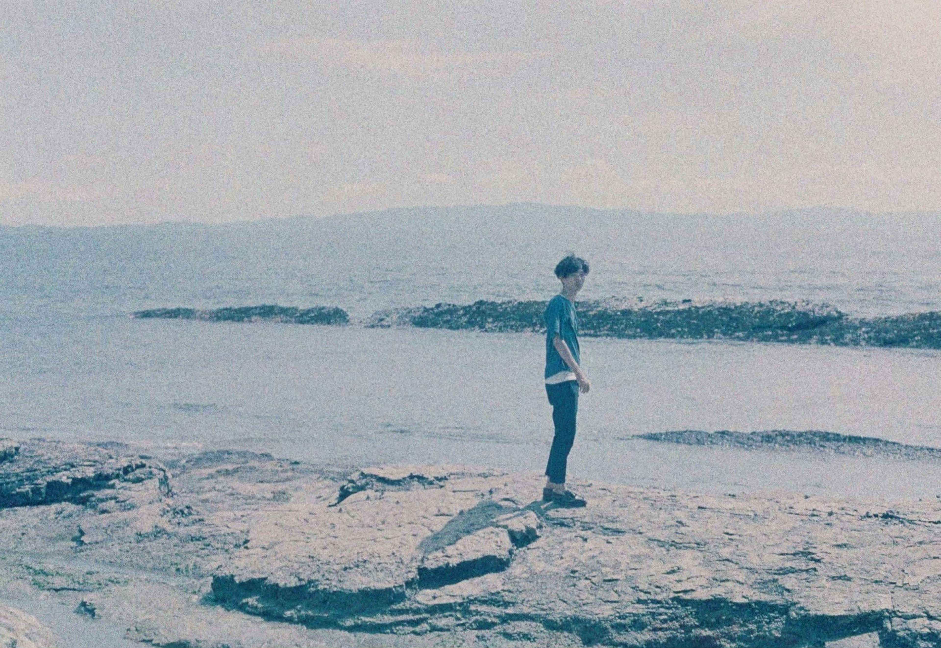 Silueta de una persona joven de pie sobre rocas costeras con mar y cielo azul