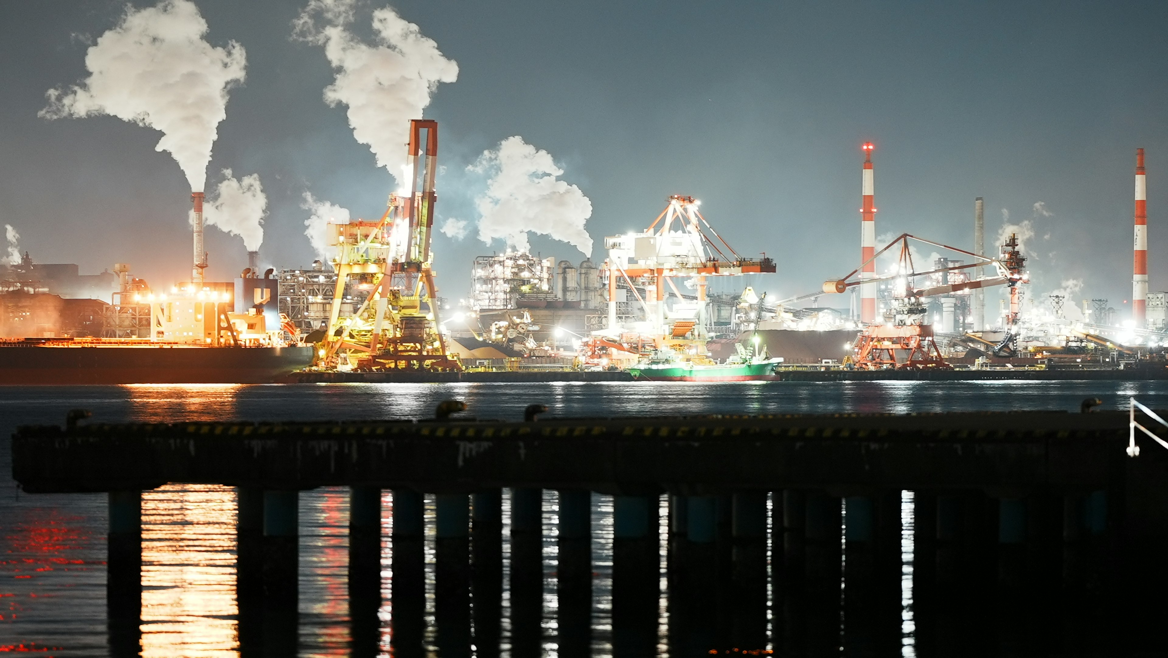 Night view of an industrial area with smokestacks and factories emitting smoke and light