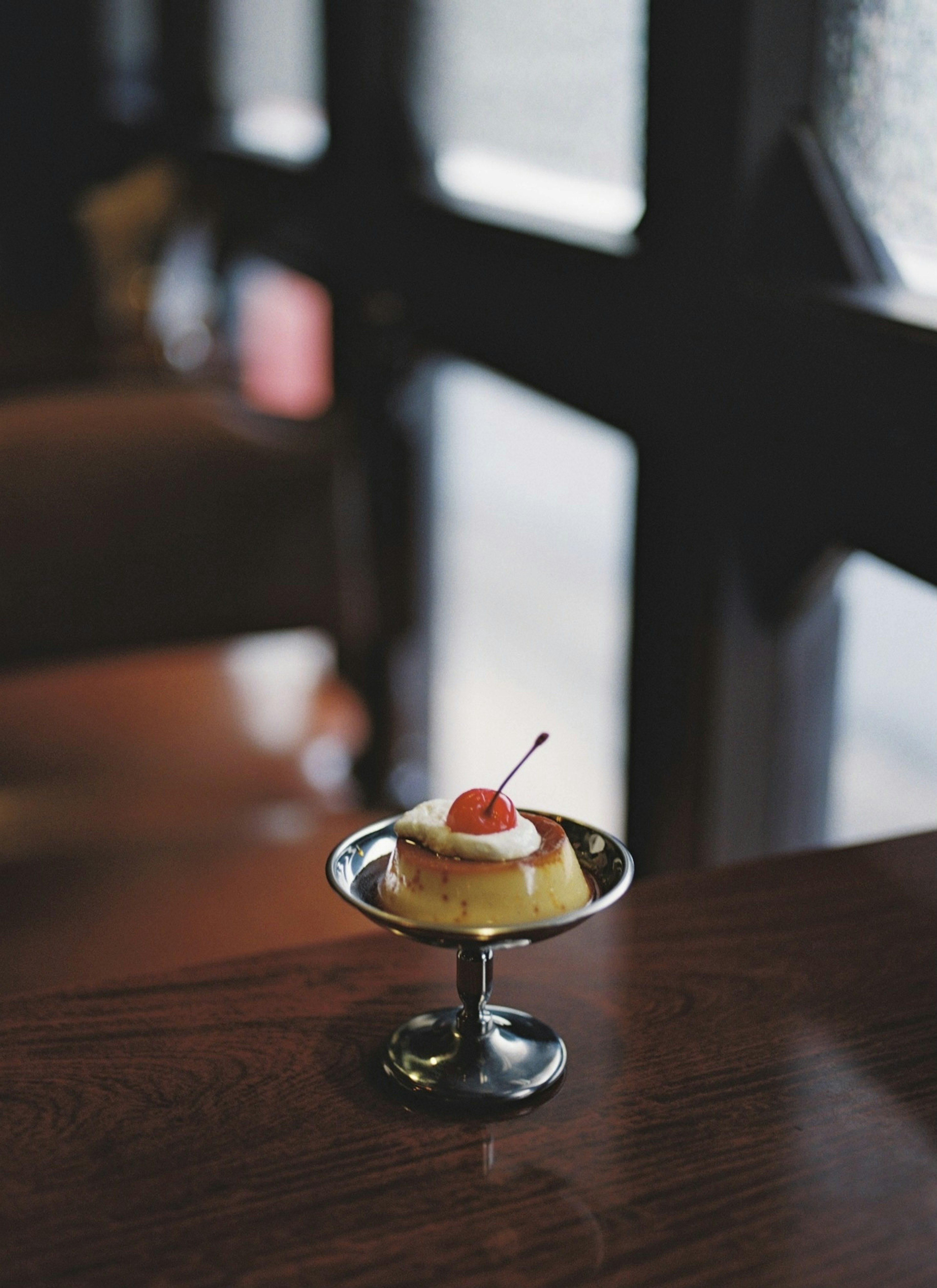 Petit verre de dessert sur une table surmonté d'une cerise et de la crème