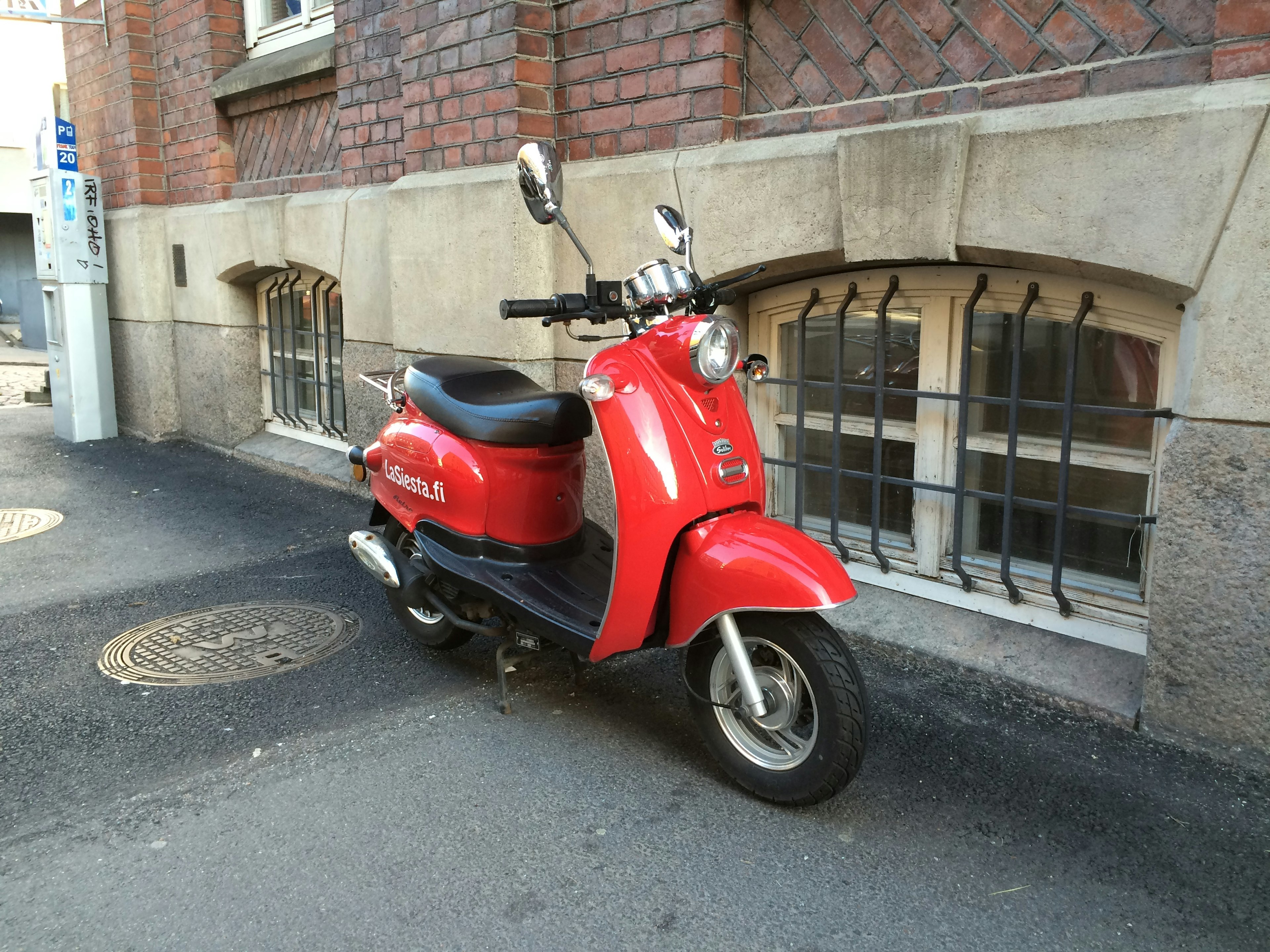 Una scooter roja estacionada junto a una pared de ladrillos