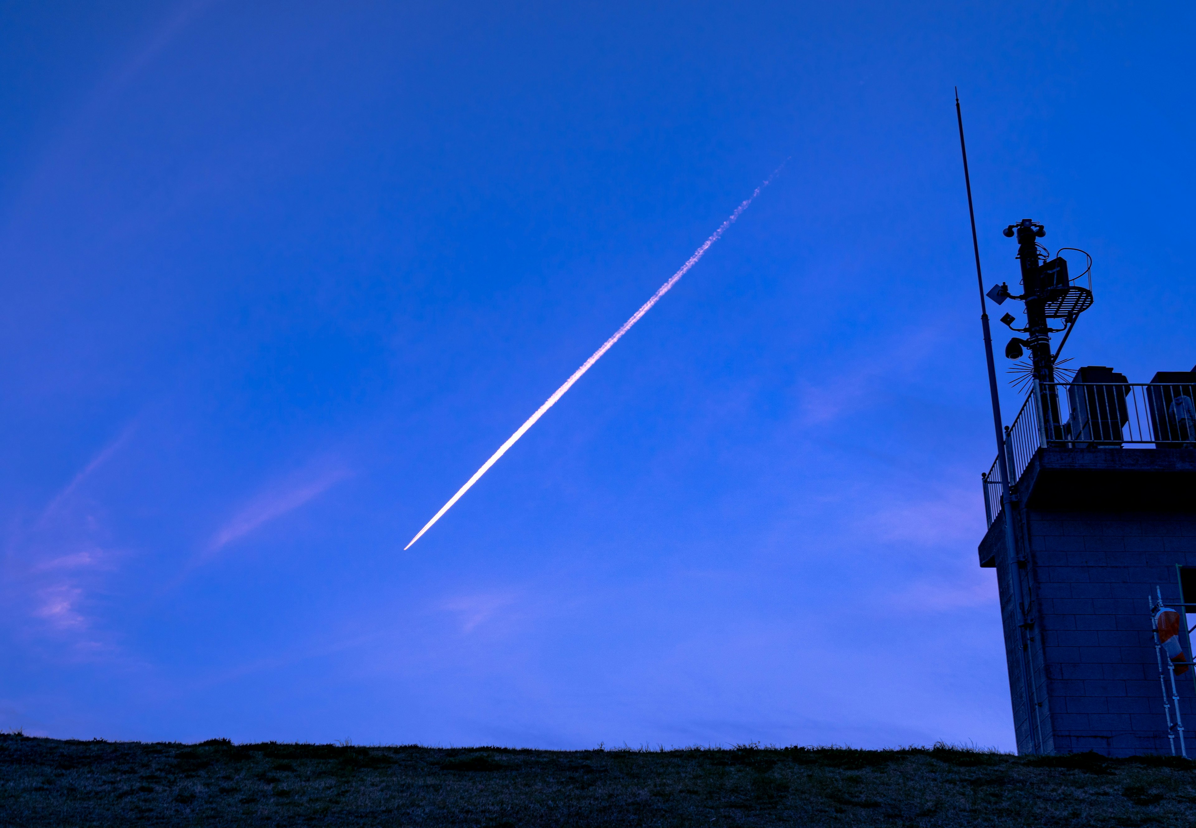 Silhouette di un edificio con una scia di aereo nel cielo blu