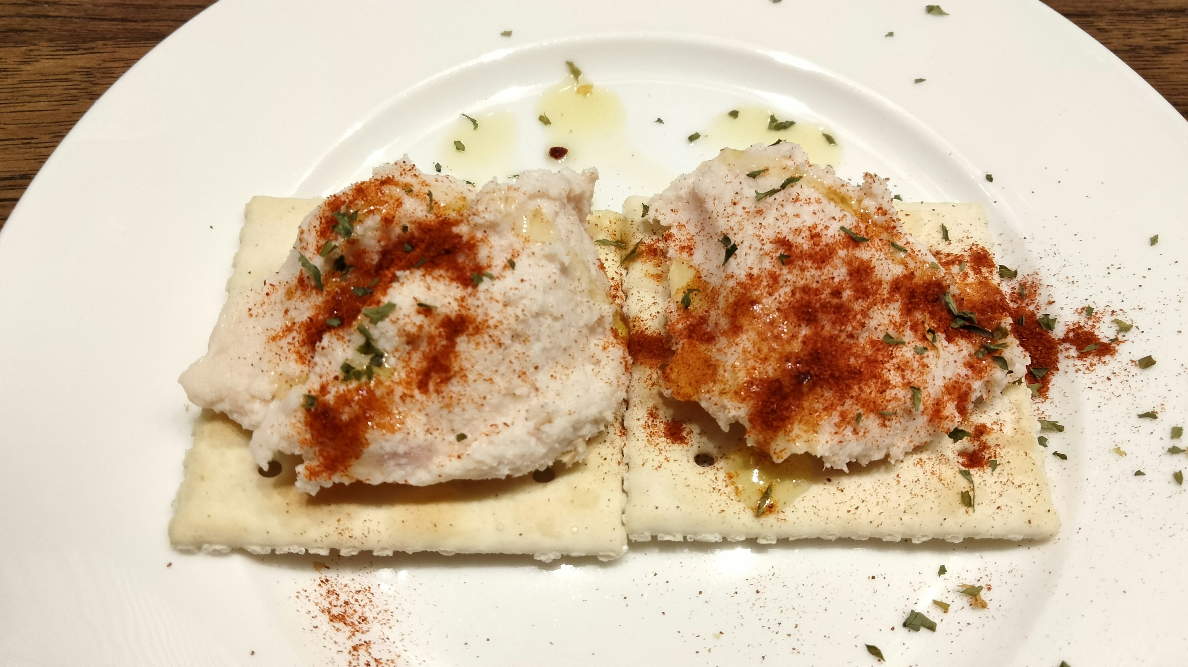 Zwei Cracker mit einer cremigen weißen Füllung bestreut mit Paprika und Kräutern auf einem weißen Teller