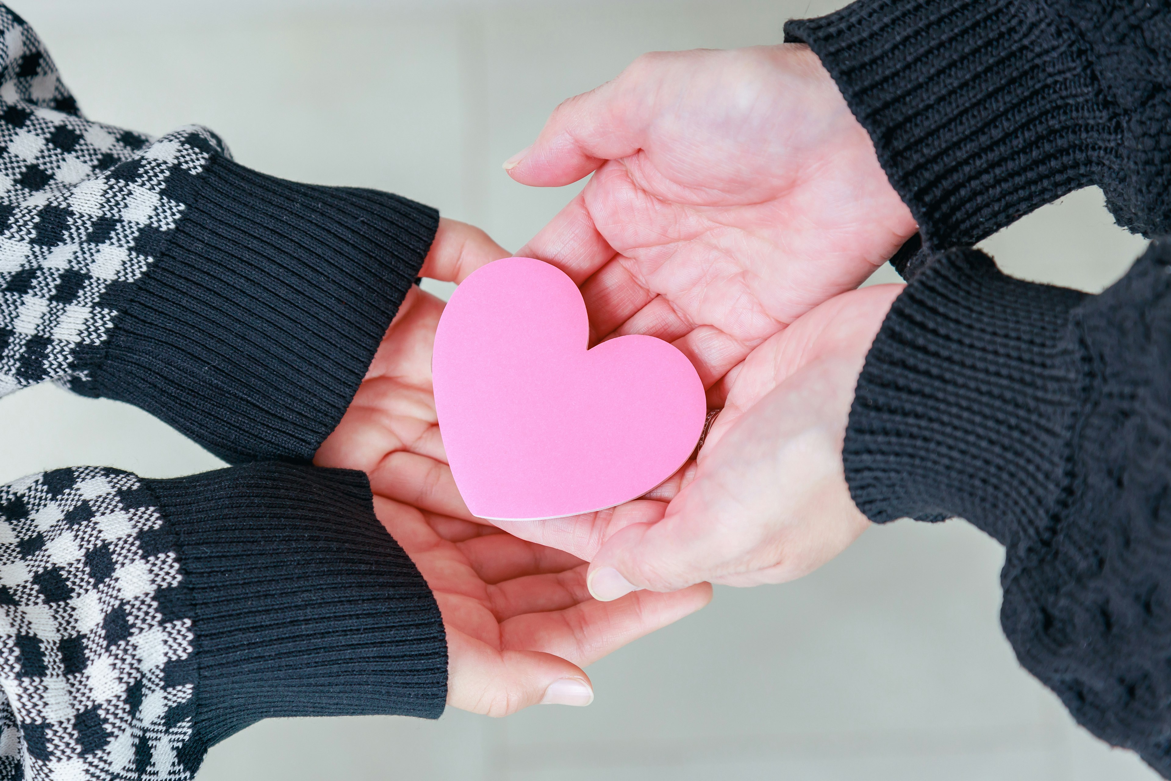 Due mani che tengono una forma di cuore rosa nei palmi