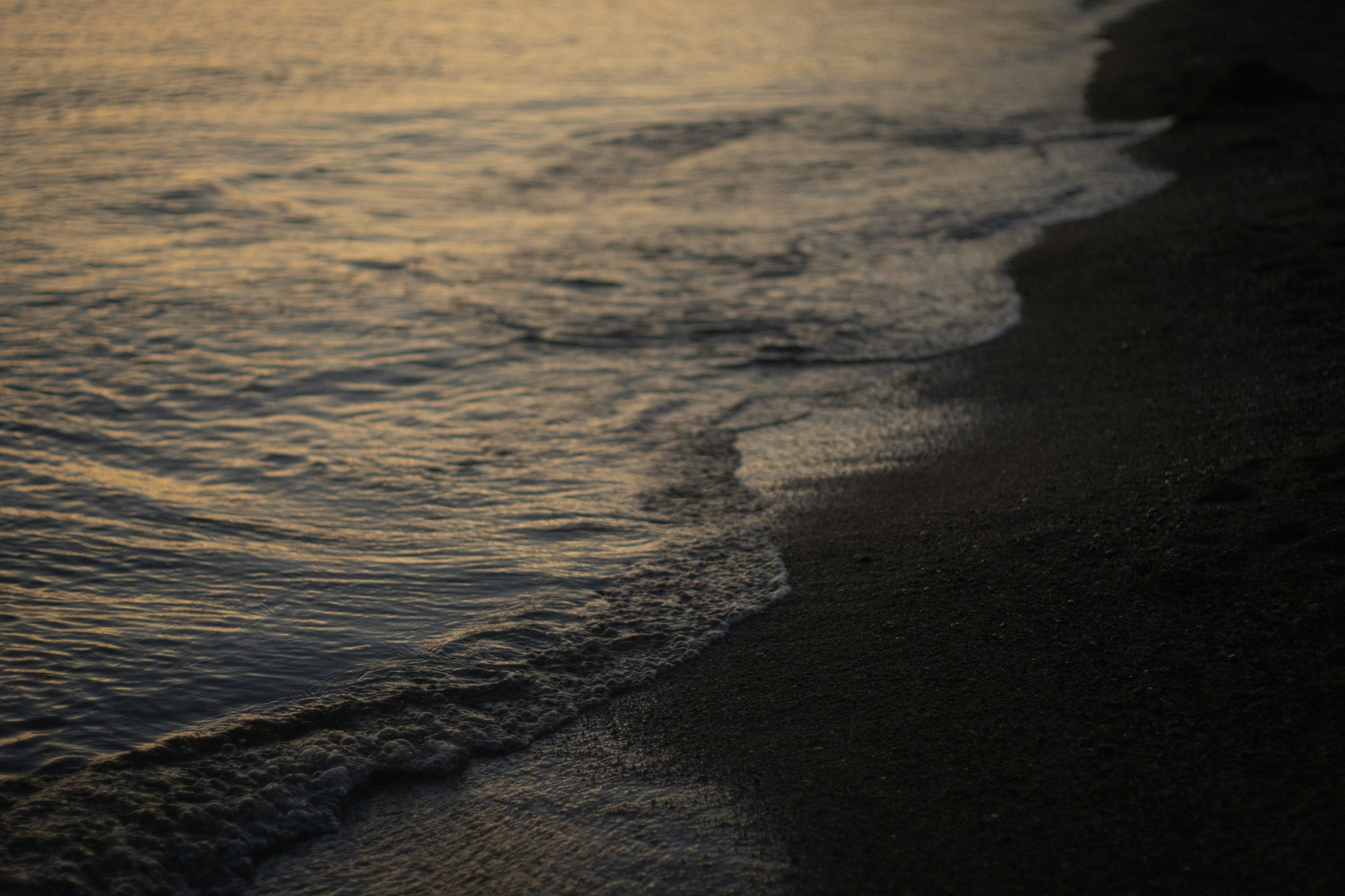 Sanfte Wellen, die am Sandstrand bei Sonnenuntergang plätschern