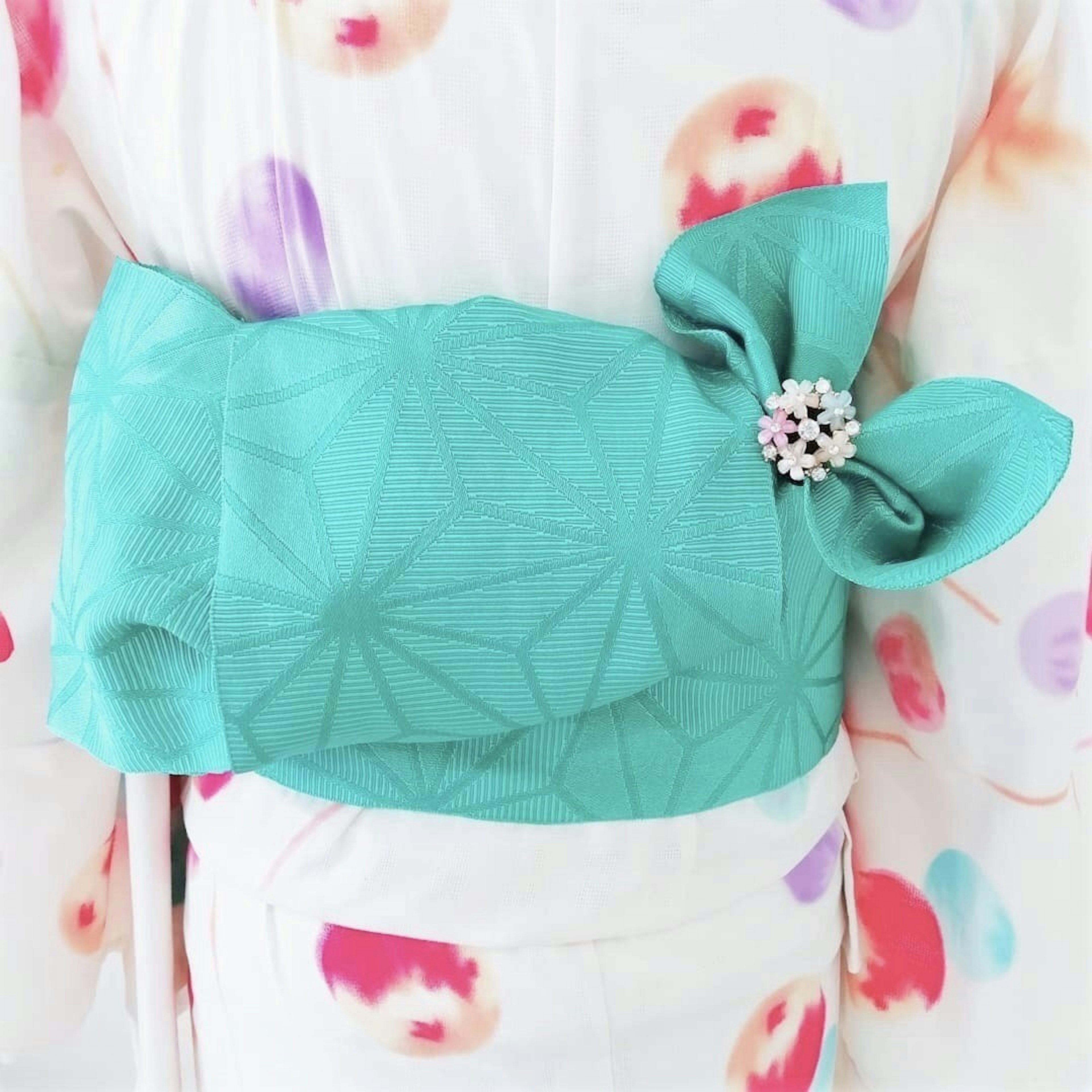 Kimono detail featuring a turquoise obi and floral accessory