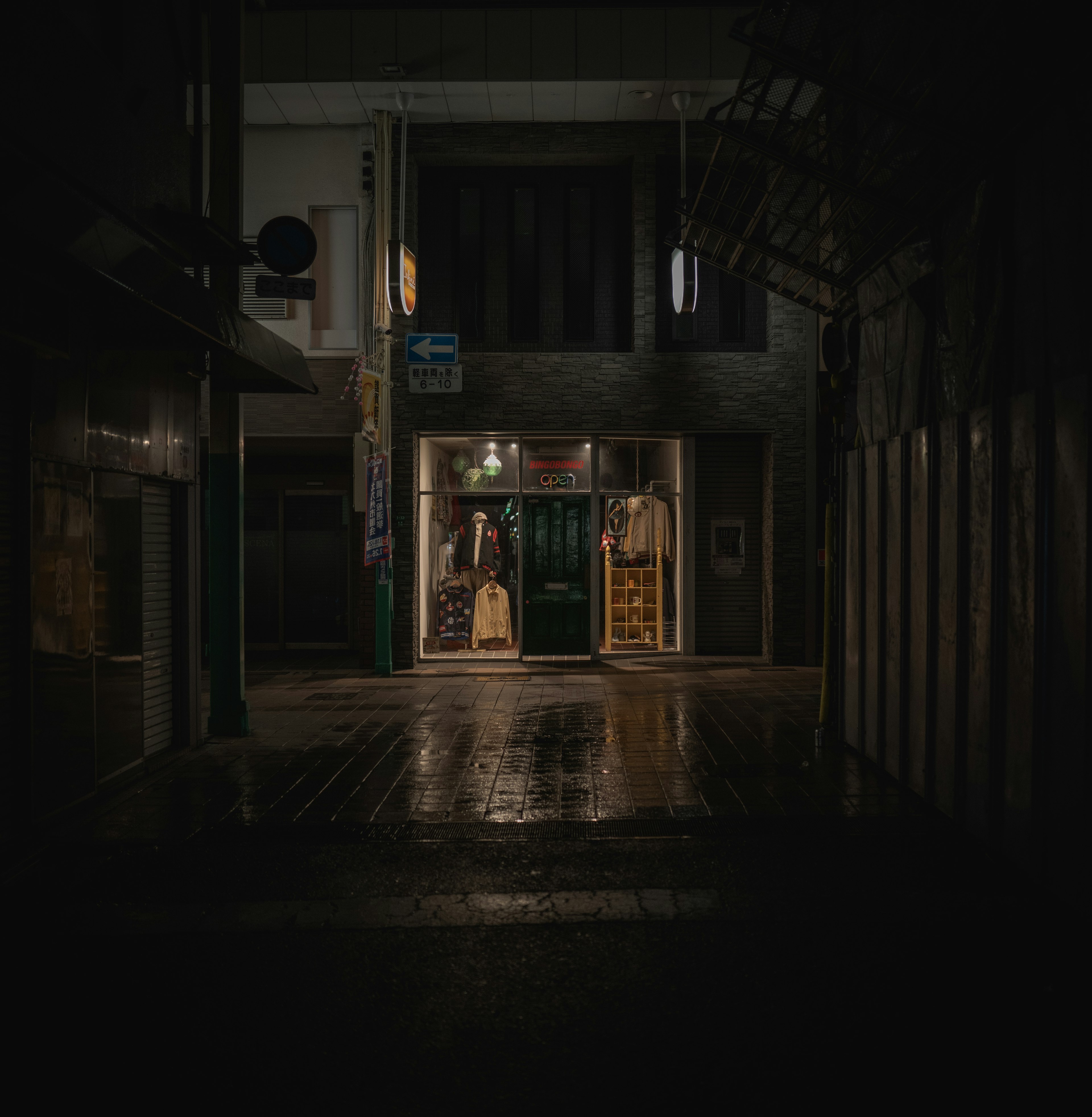 Una entrada de tienda visible en una calle oscura en una escena nocturna lluviosa