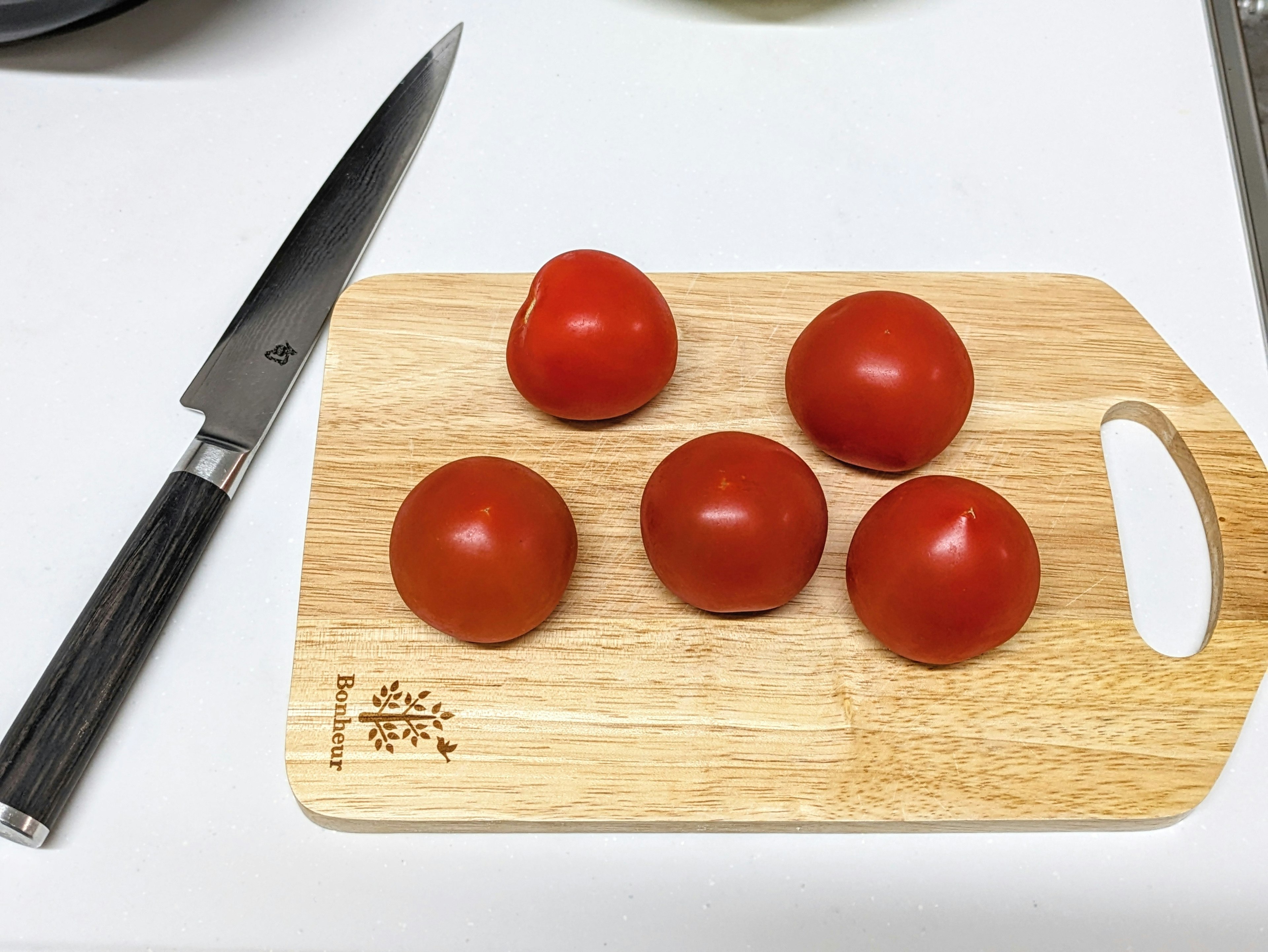 Five red tomatoes arranged on a wooden cutting board