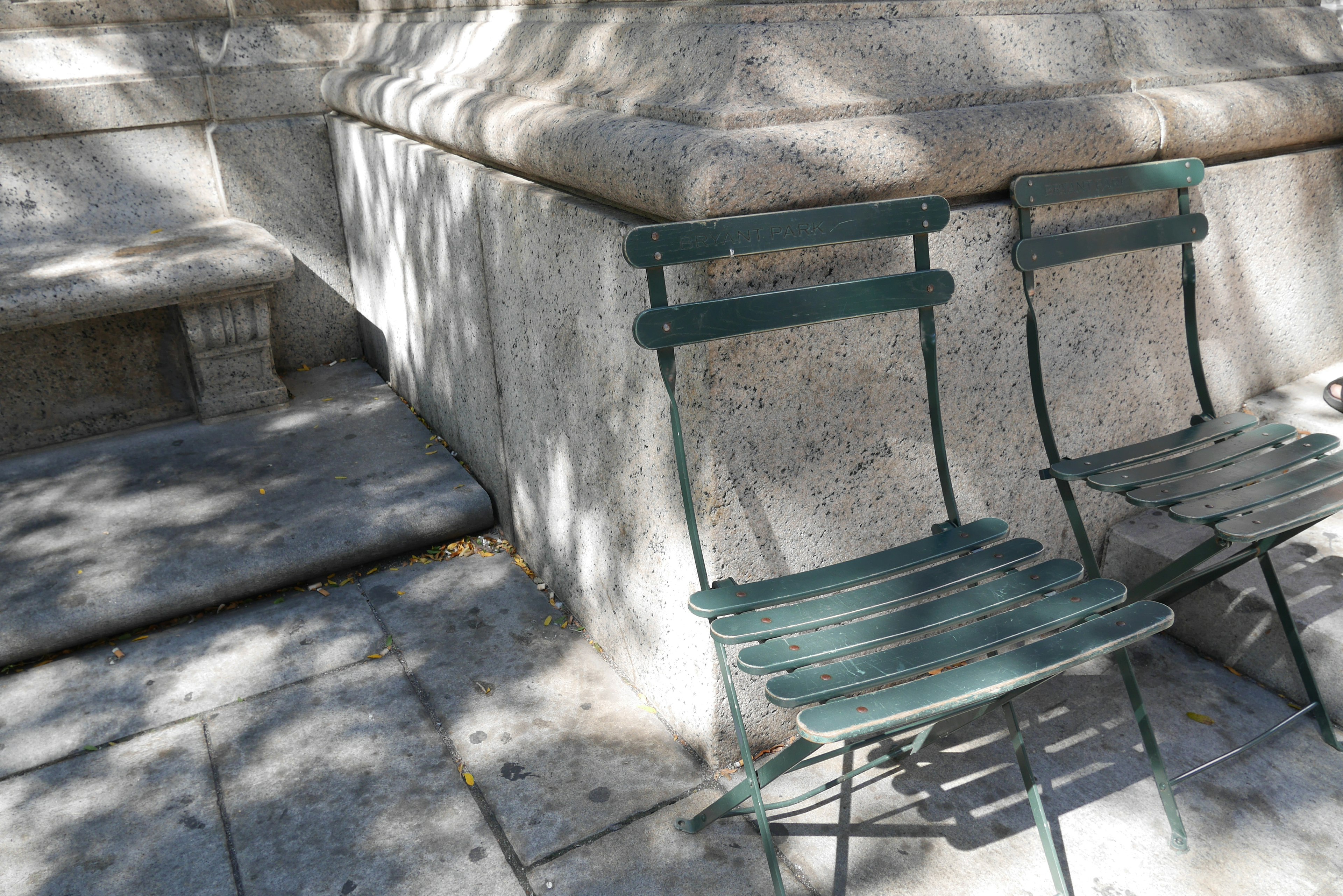 Deux chaises vertes à côté d'un mur en pierre avec des ombres de lumière