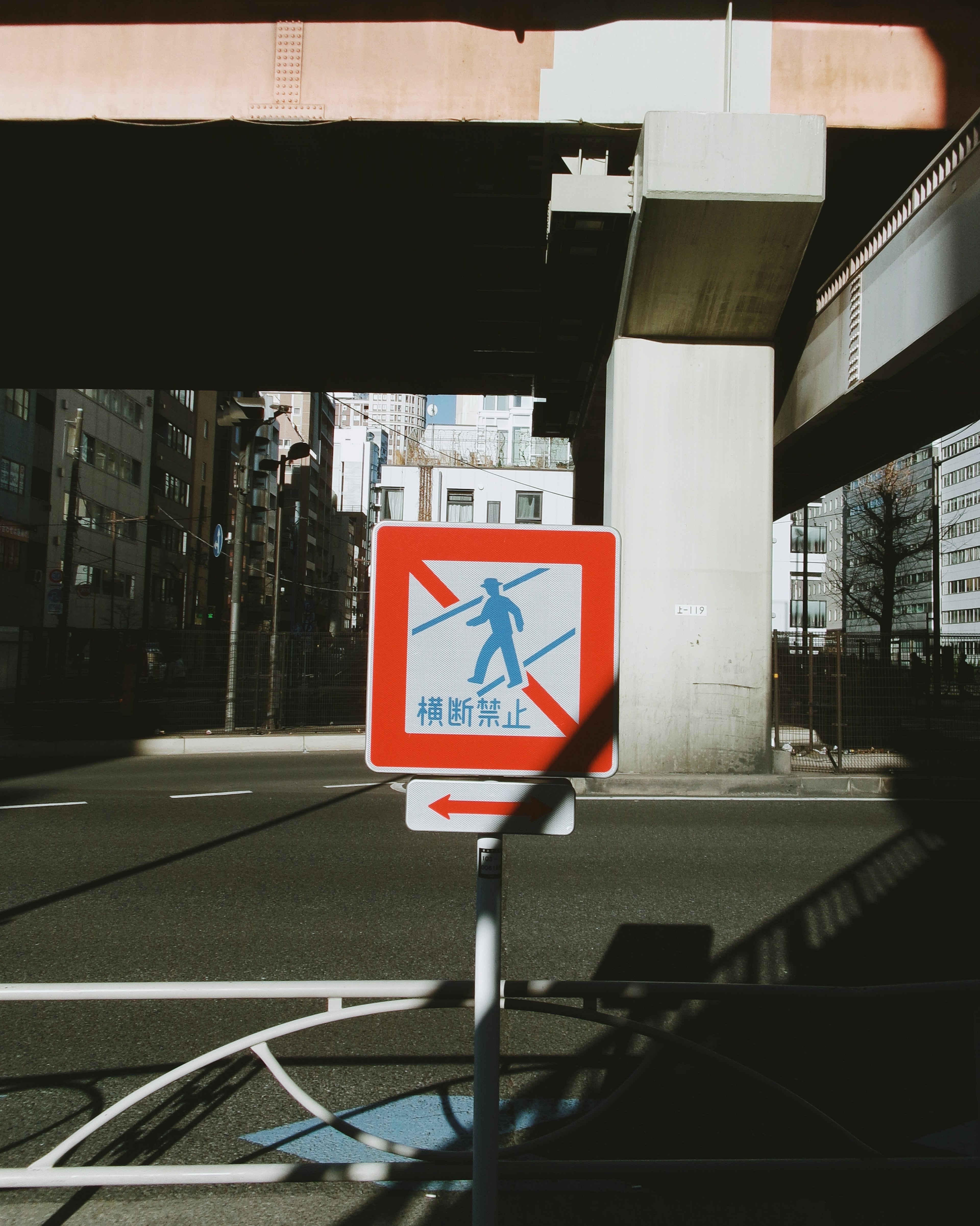 赤い矢印のある歩行者注意の標識と高架橋の下の街並み