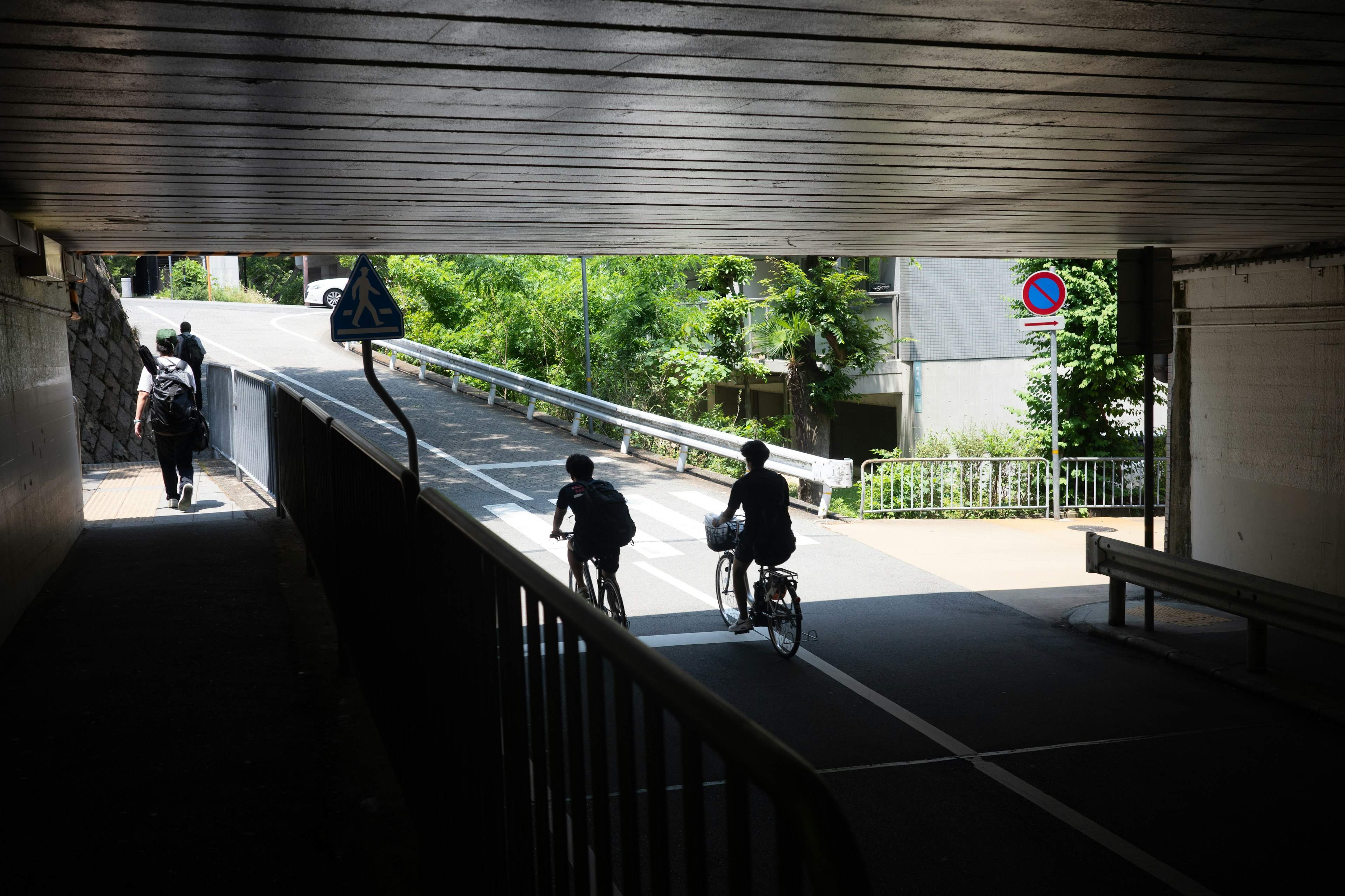 Menschen, die unter einem Tunnel gehen und Fahrrad fahren, mit Grün im Hintergrund