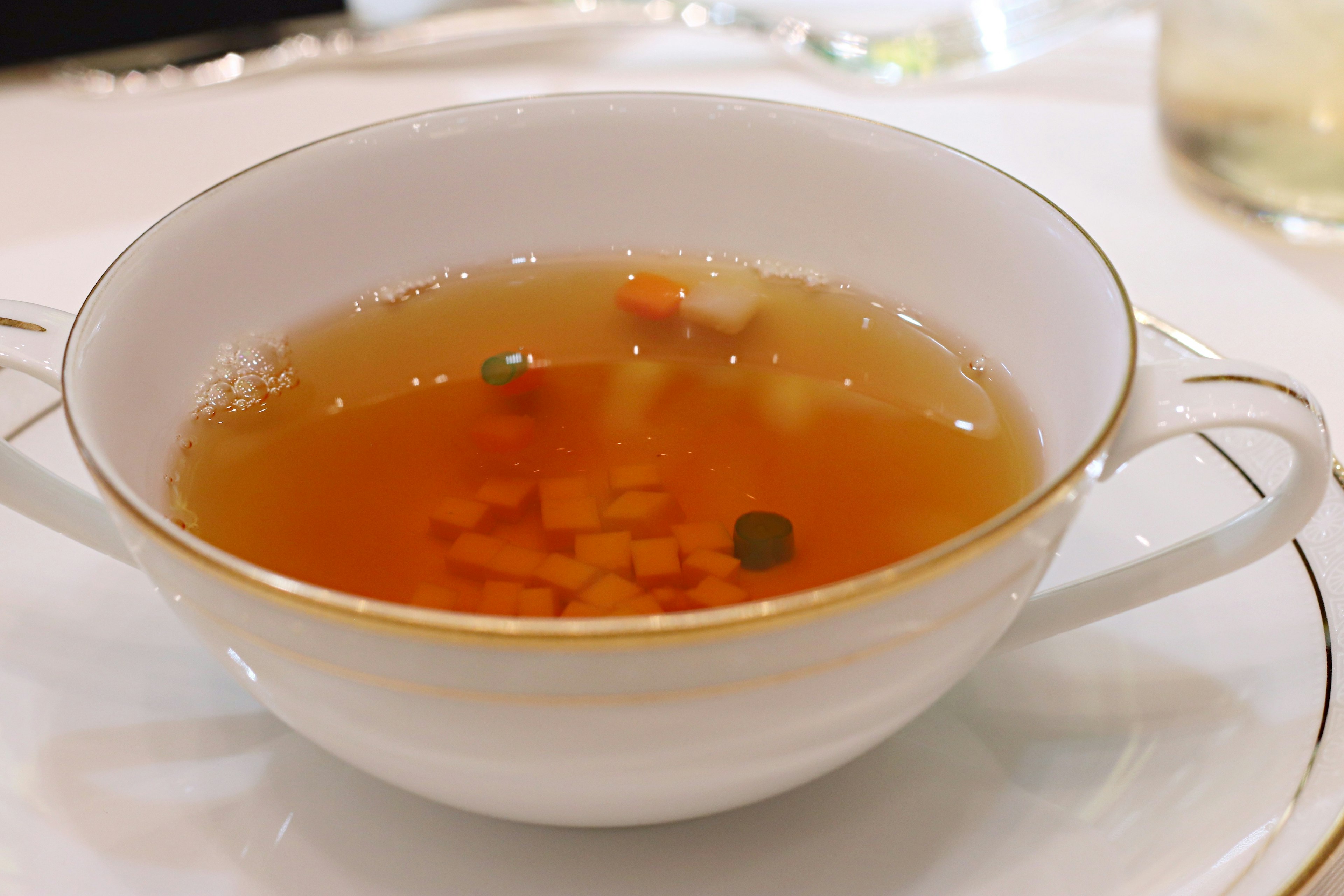 Clear soup in a white cup with colorful vegetables floating