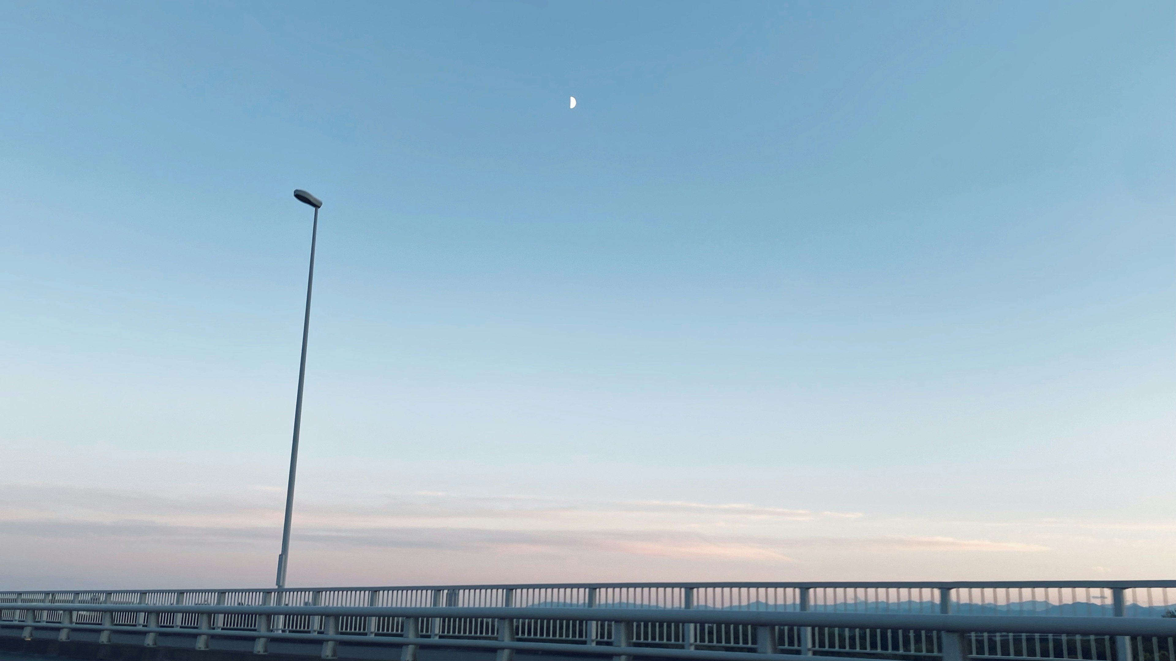 Vista de la luna en un cielo azul sobre un largo puente