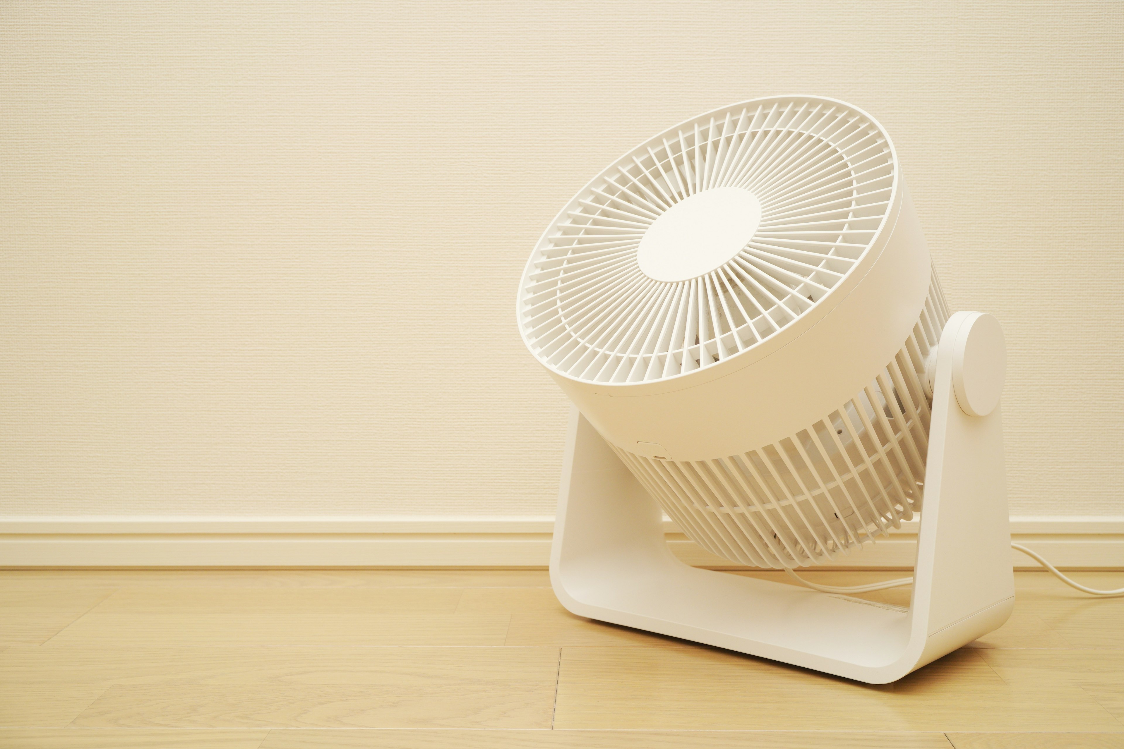 A white fan positioned on the floor against a simple backdrop