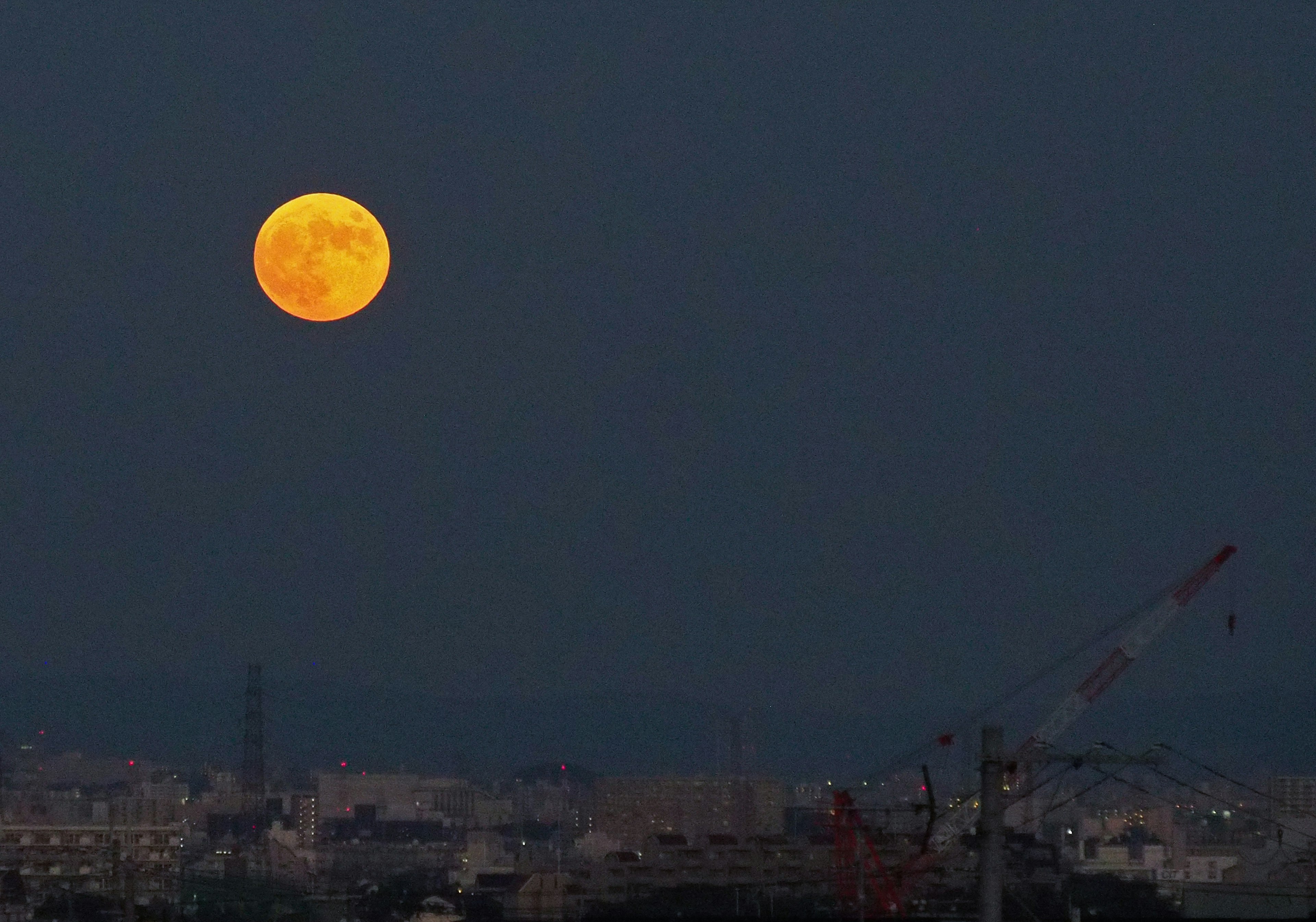 Orangefarbene Vollmond im dunklen Himmel mit Stadtsilhouette