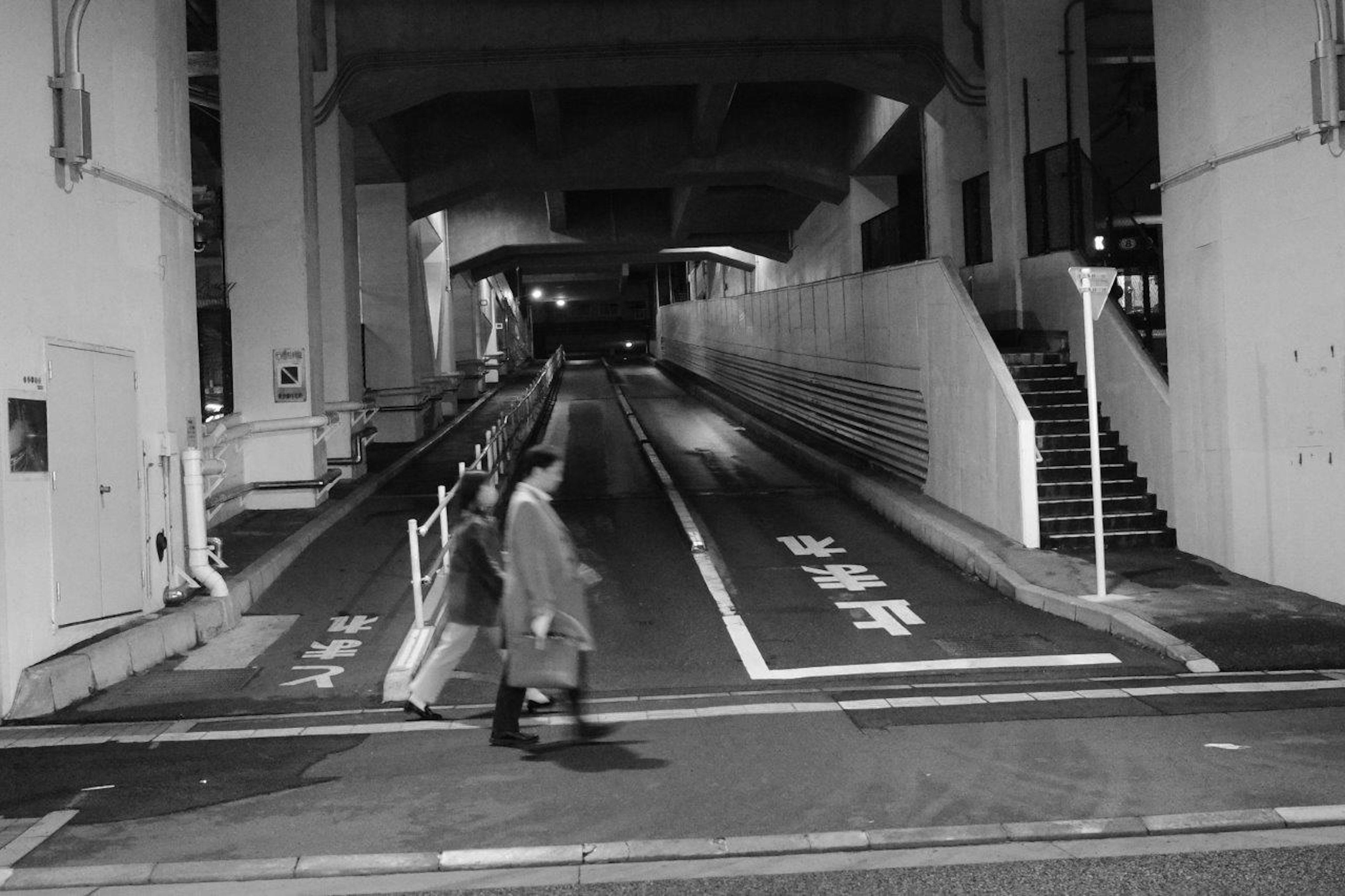 People walking in a city at night under a concrete overpass