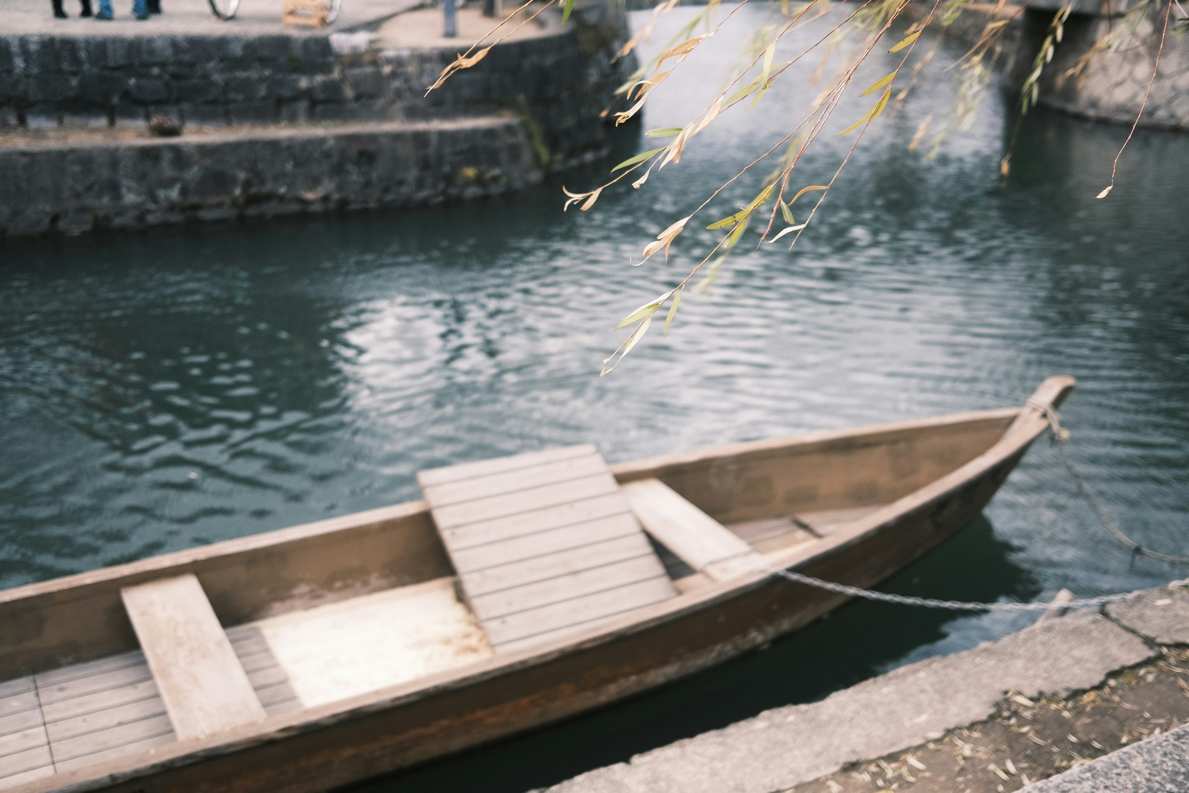 Bote de madera flotando en agua tranquila con borde de piedra y árboles