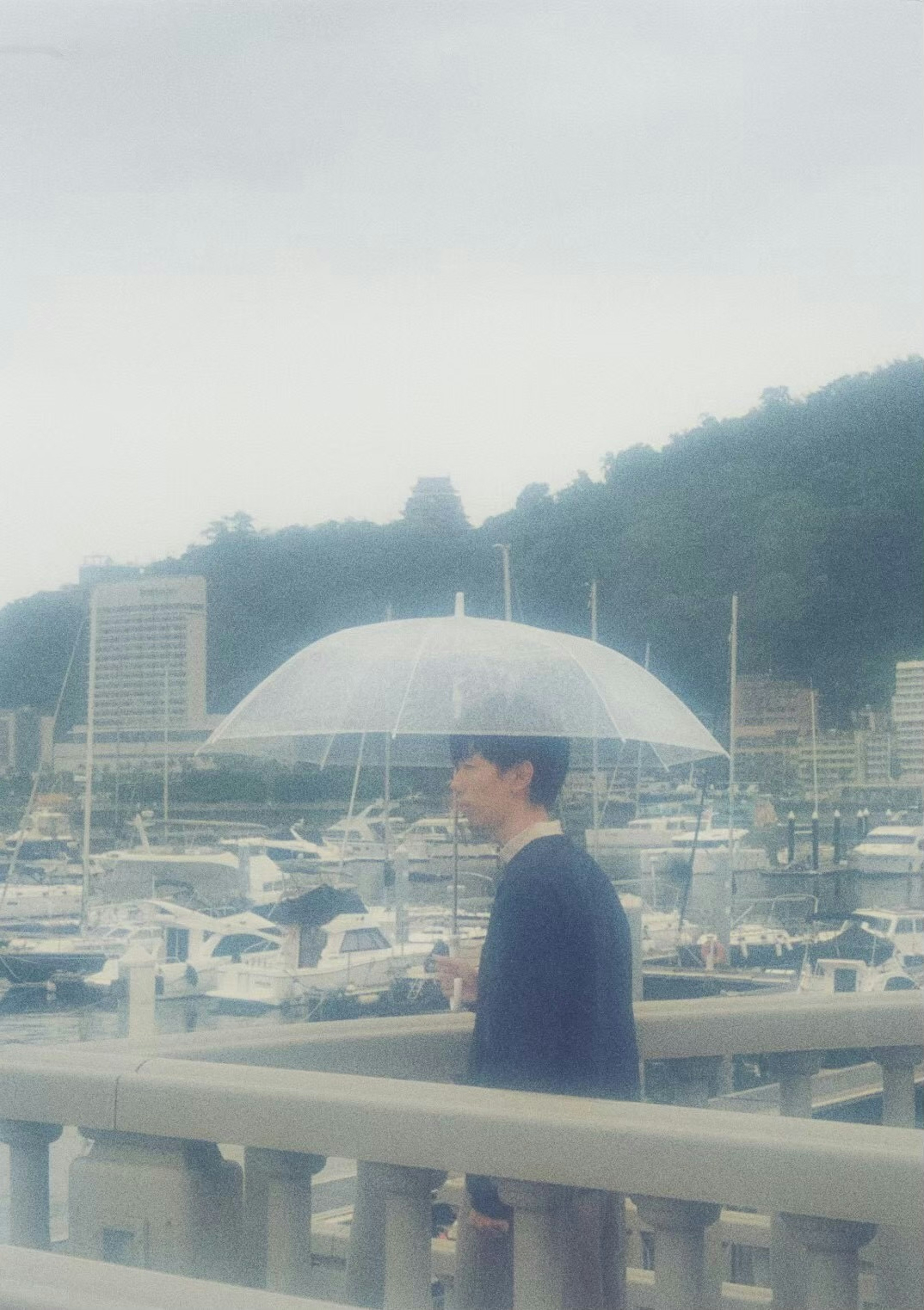 A man walking on a pier holding a transparent umbrella