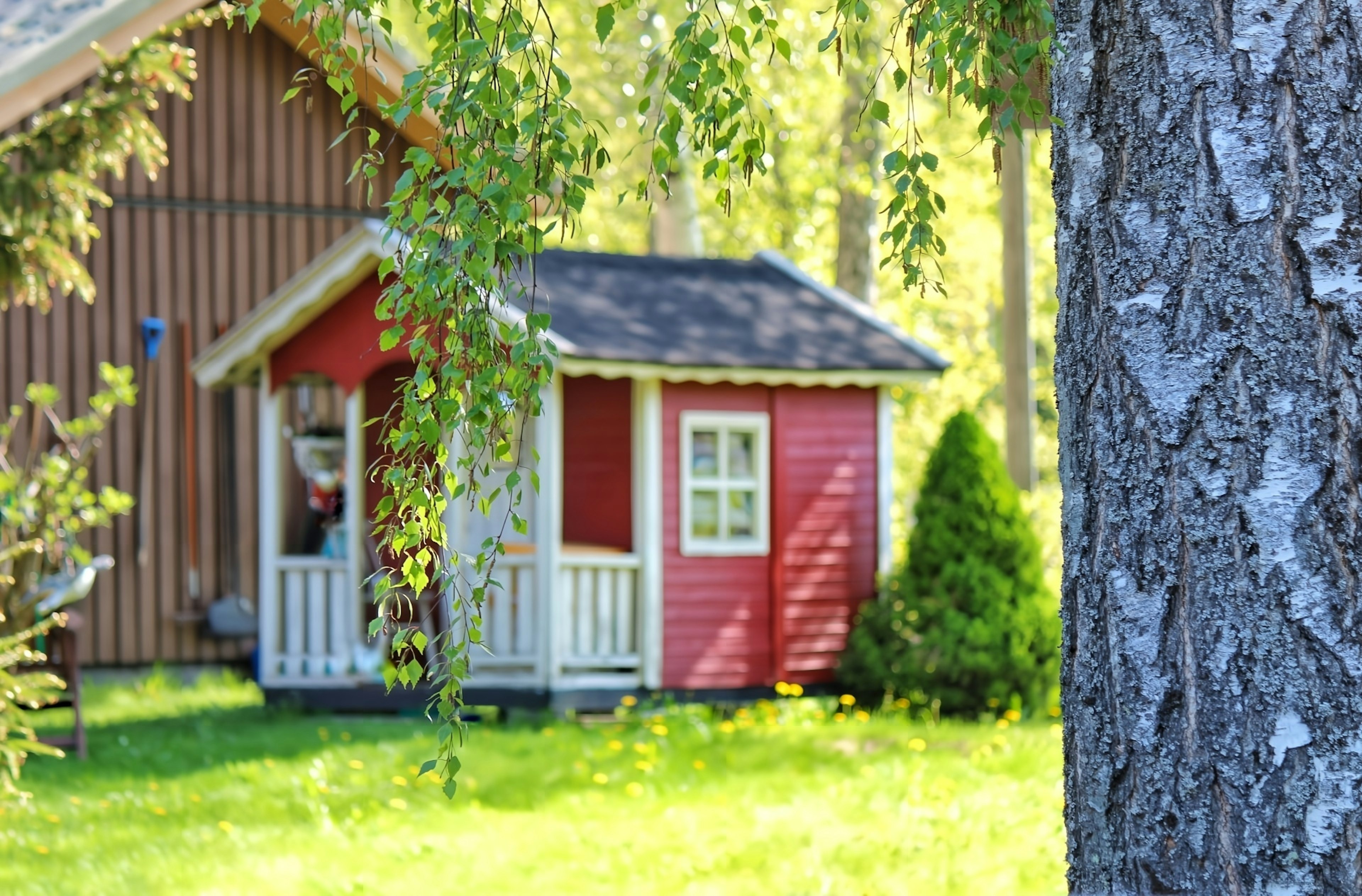 A red cottage surrounded by green grass and trees in the background