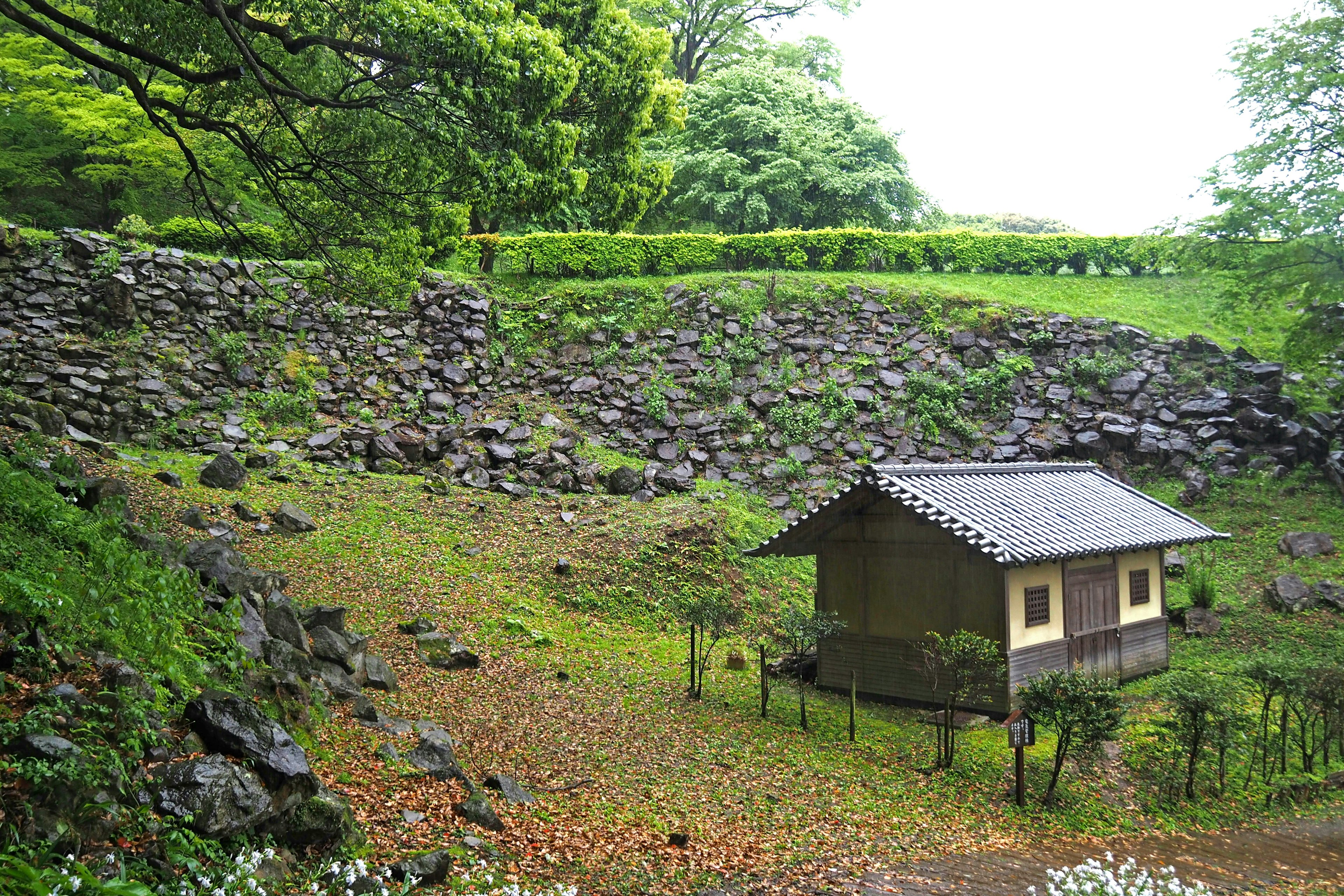 石垣と緑の木々に囲まれた小さな家