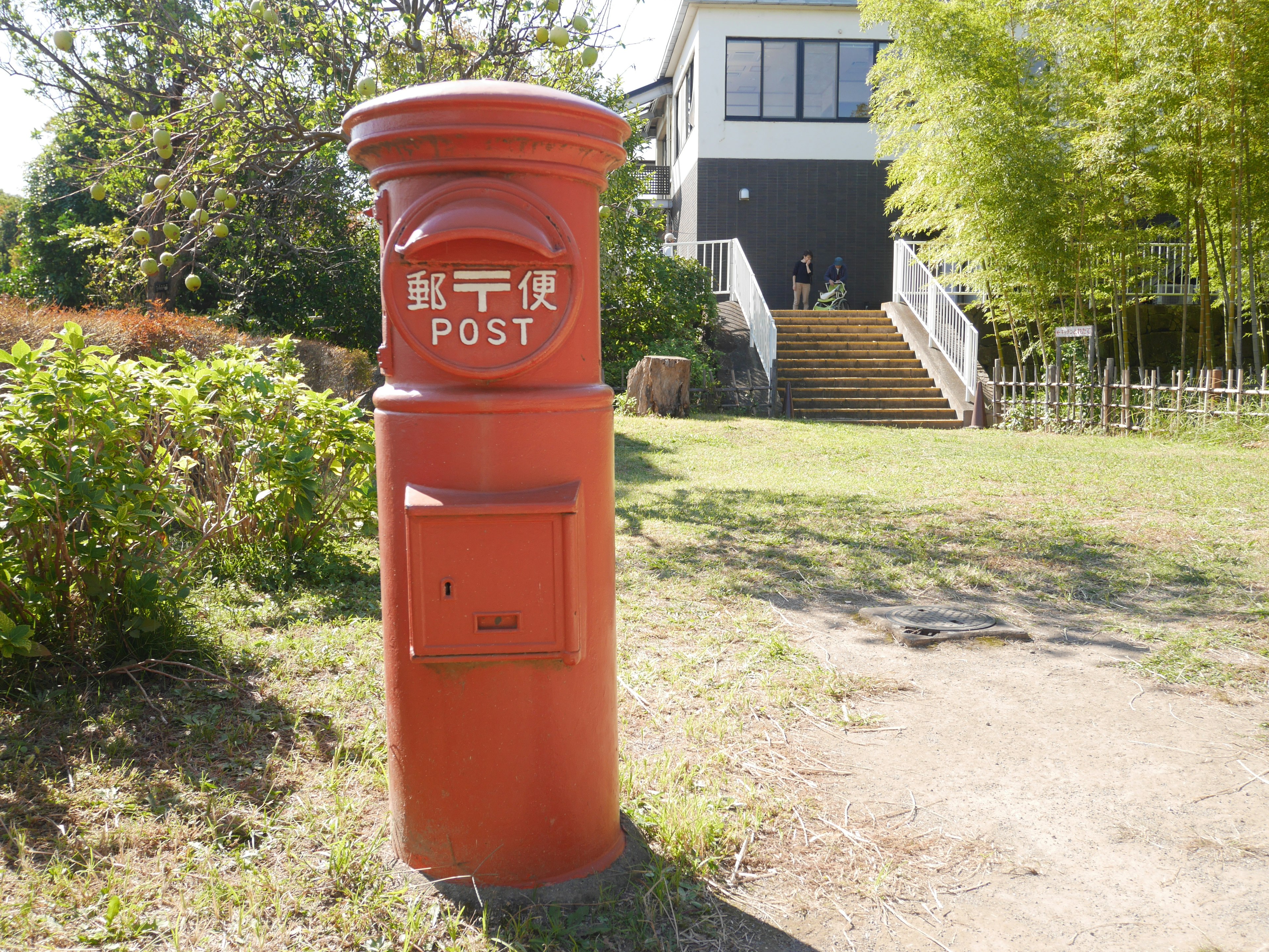 Roter Briefkasten in einem Garten mit einem Gebäude und Bambus im Hintergrund