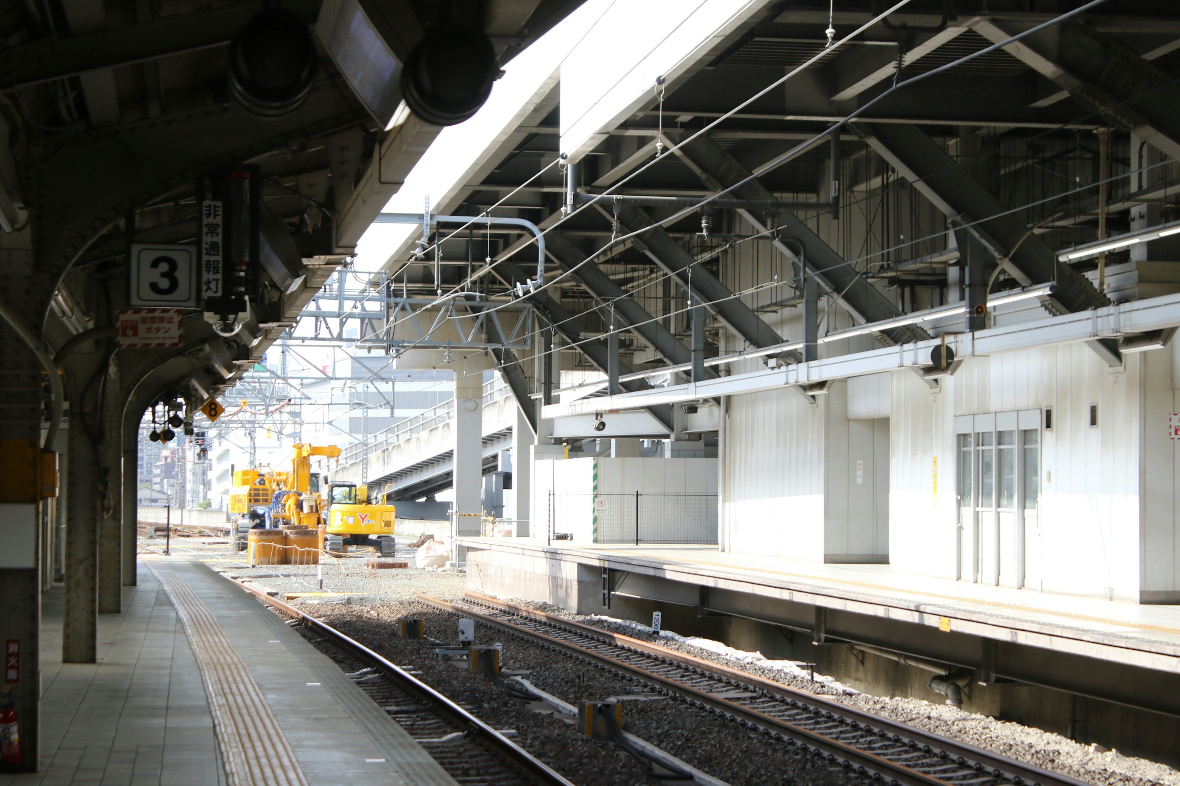 View of a train platform with tracks and a construction yellow machine