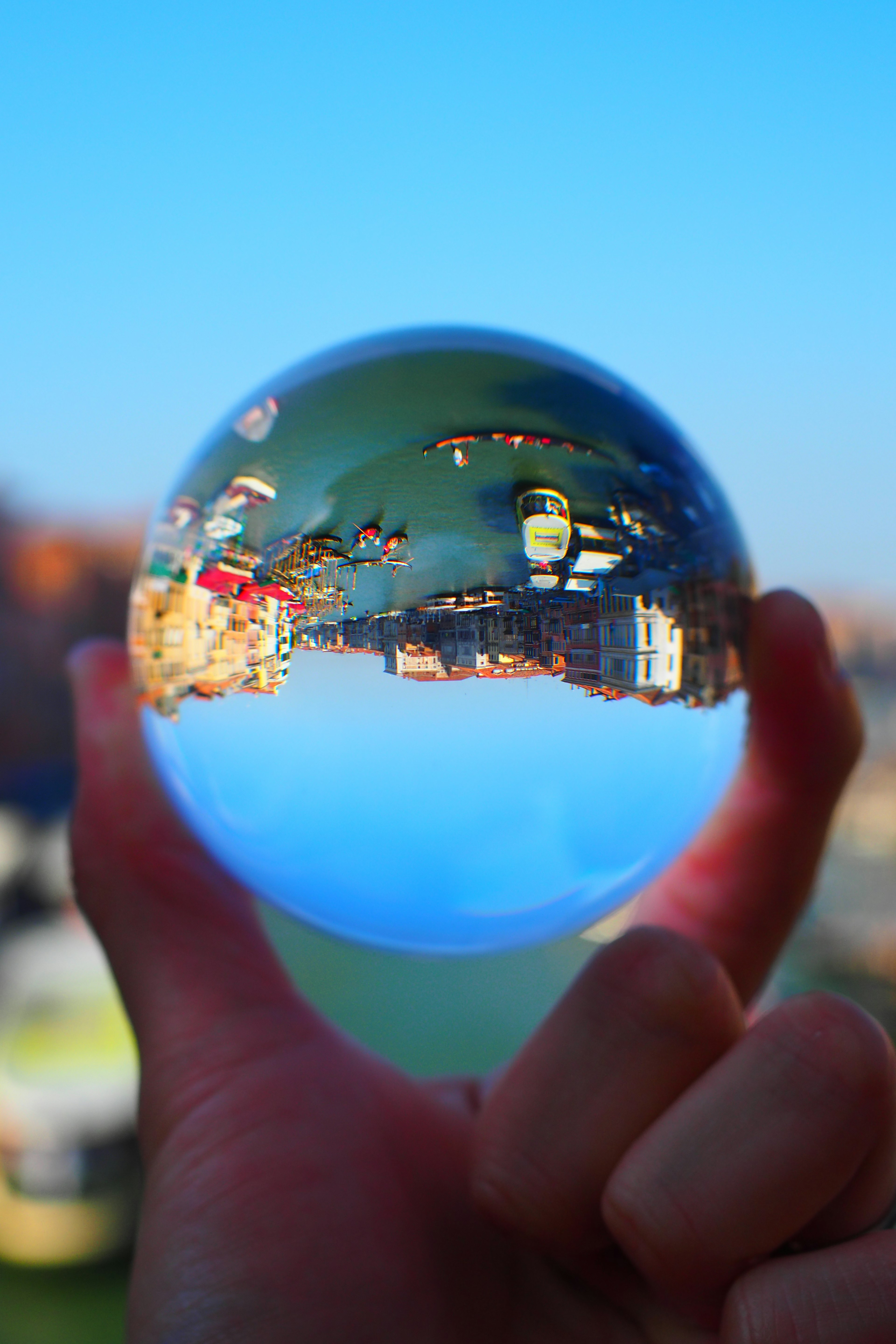 A clear glass sphere held in hand reflecting blue sky and cityscape