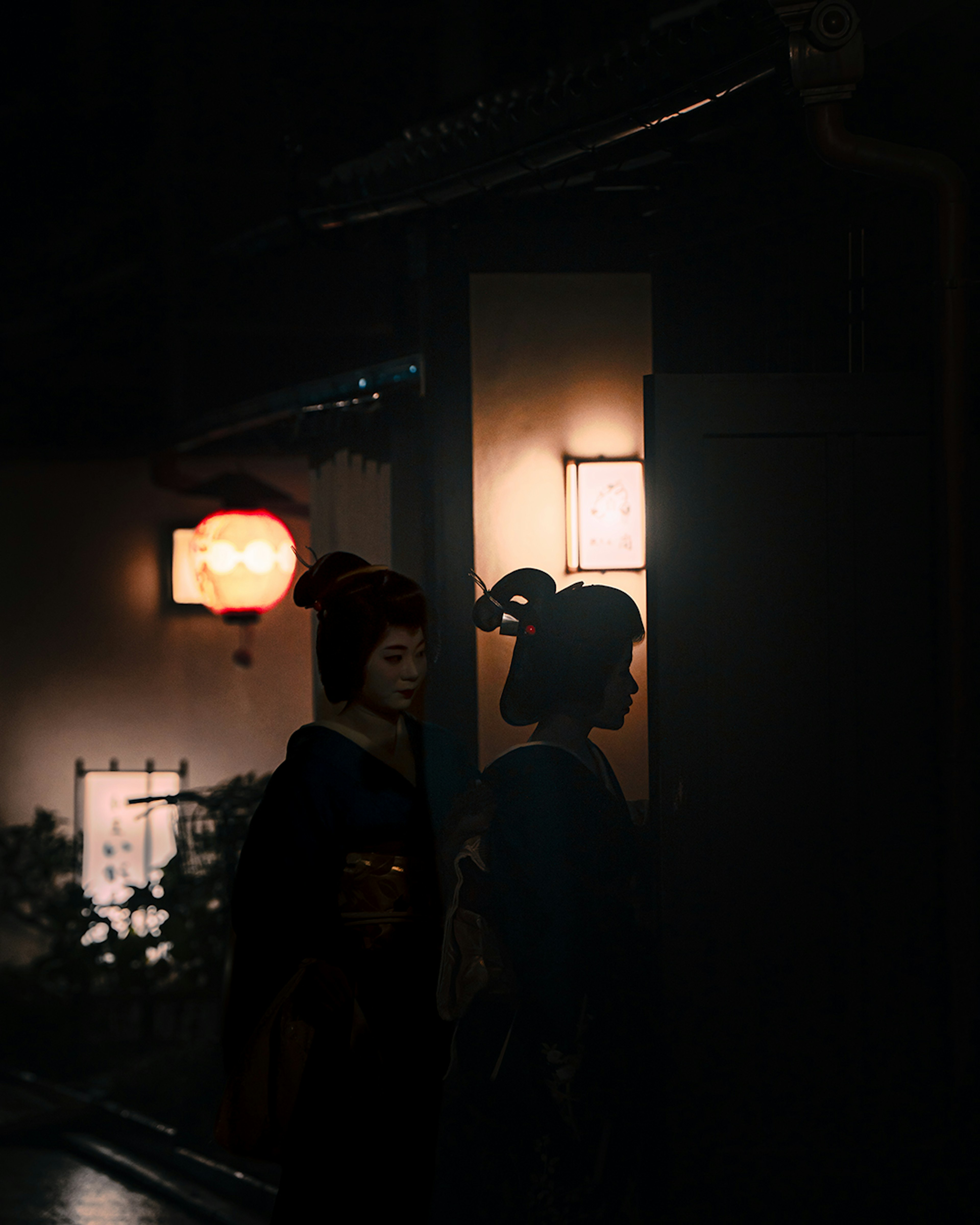 Silhouette of a woman in kimono against a dark background with lantern light