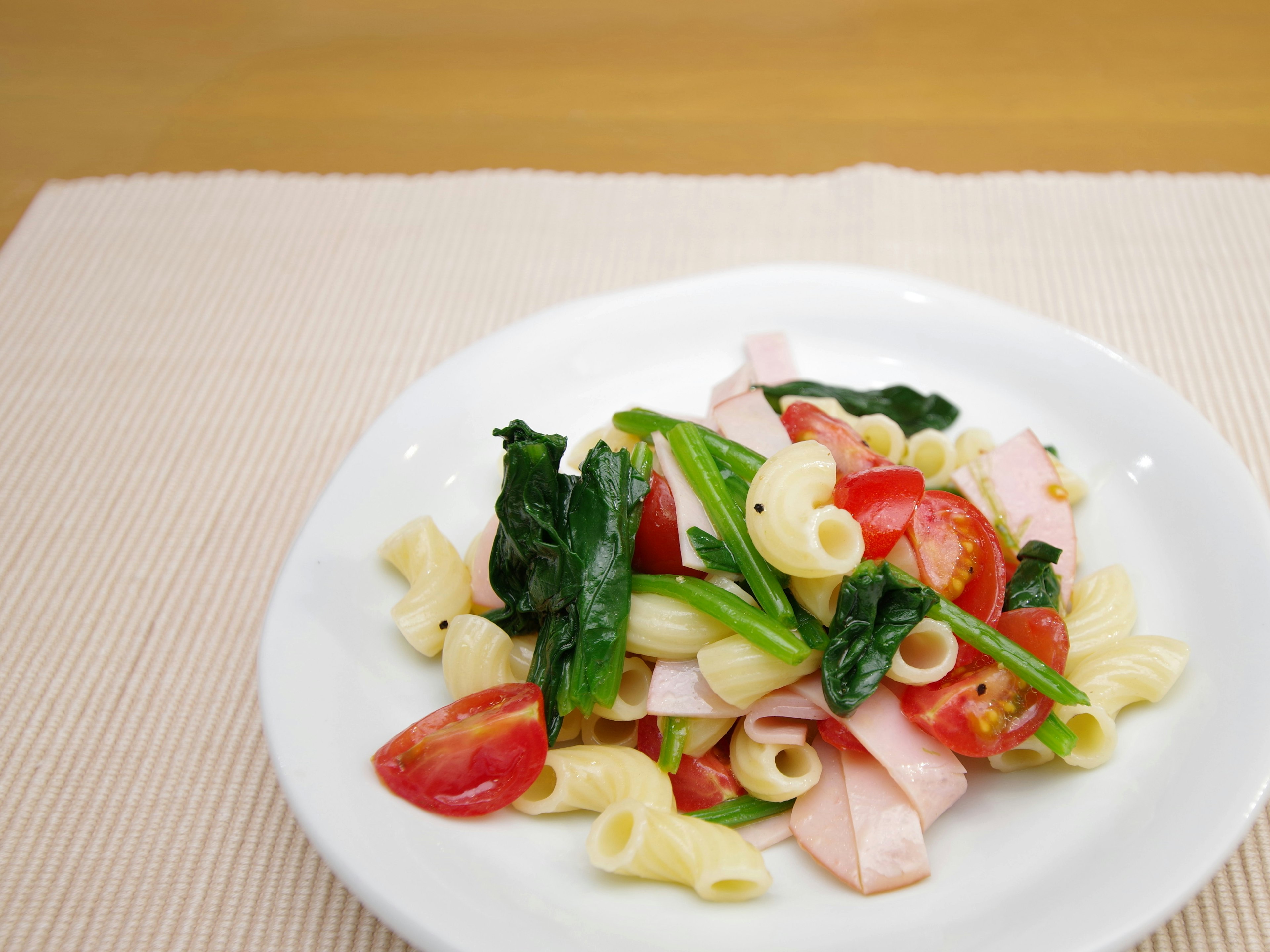 Ensalada de pasta en un plato blanco con tomates y espinacas