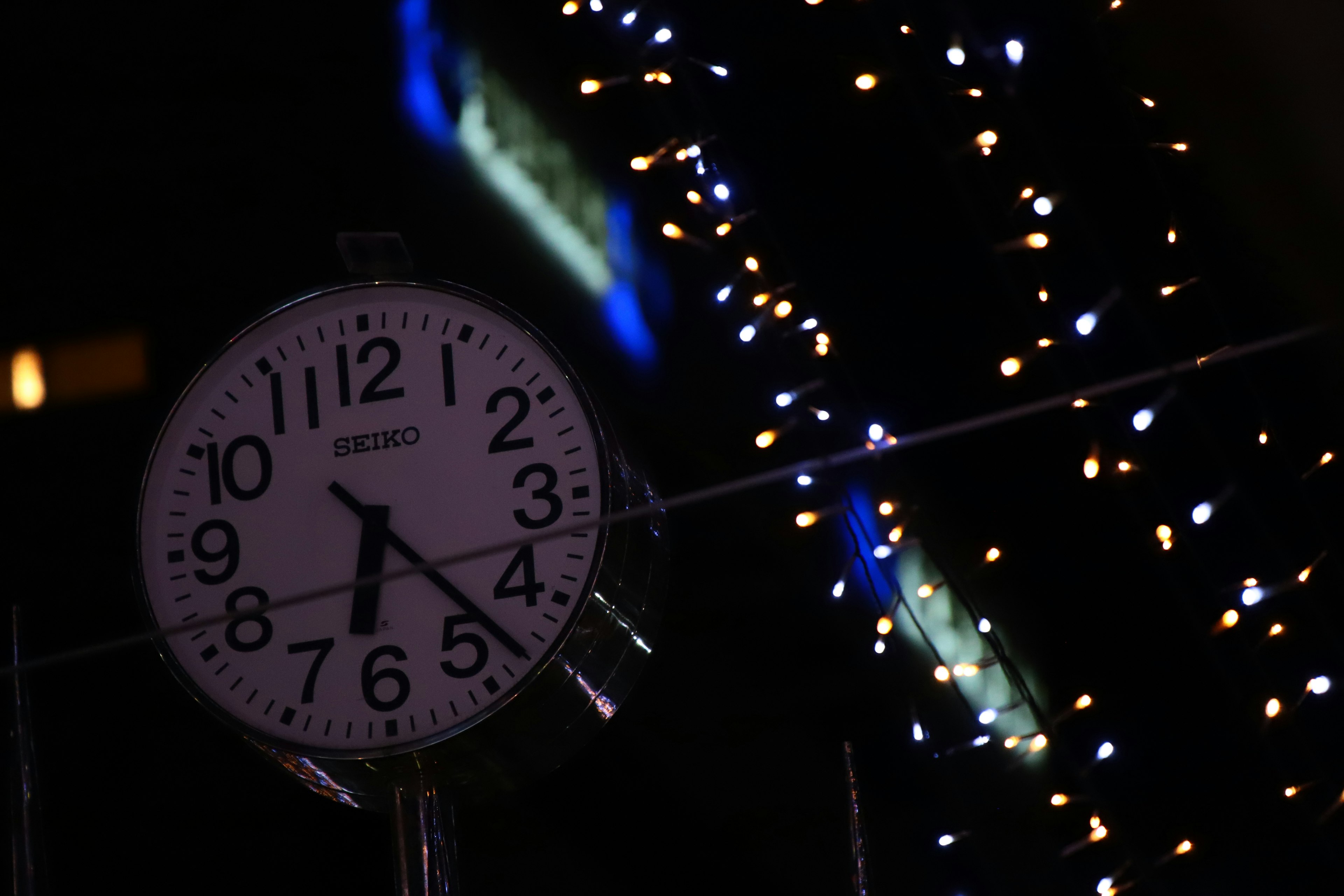 Analoge Uhr an einer Straßenecke mit bunten Lichtern bei Nacht