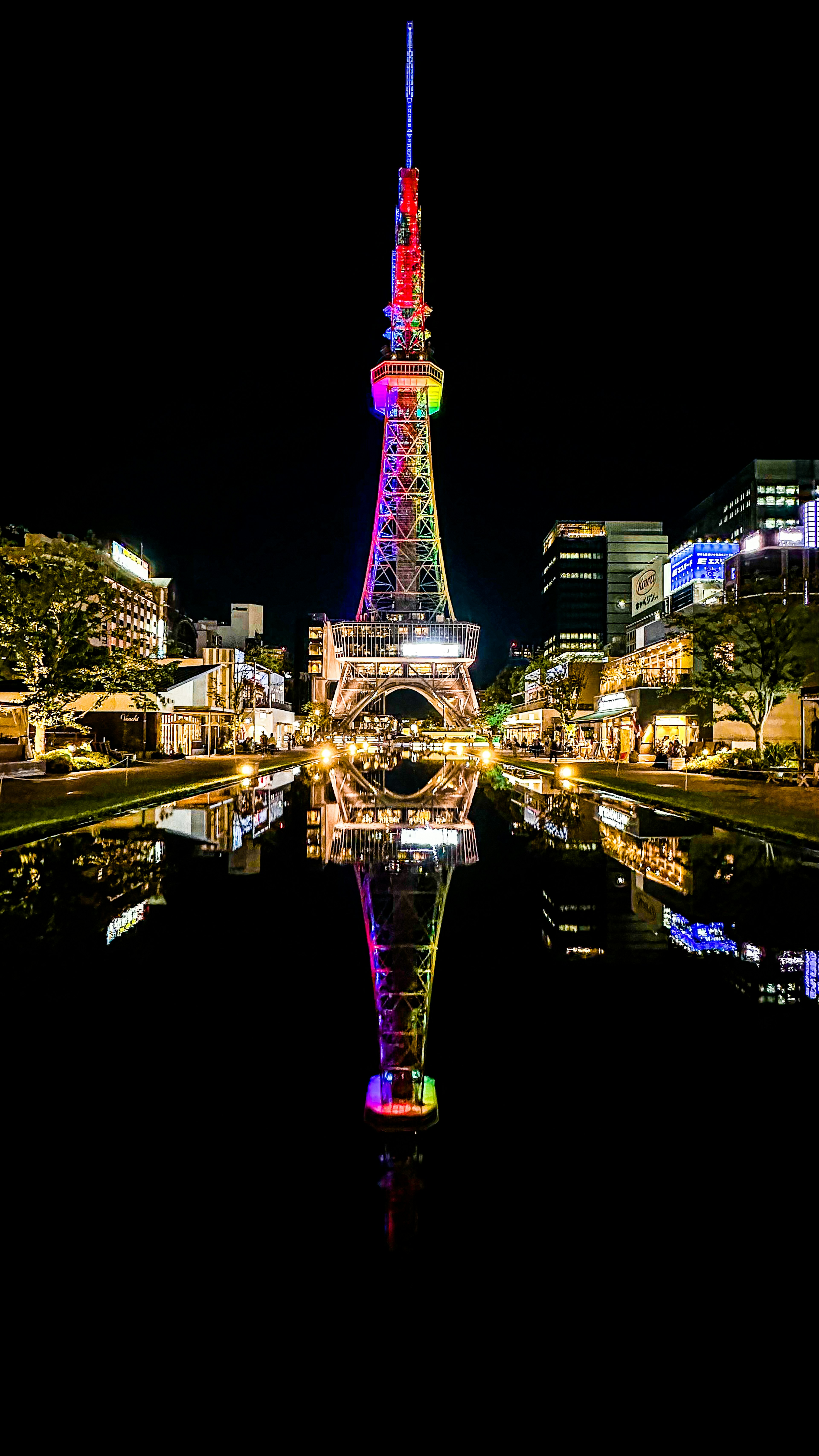 Nagoya Fernsehturm bei Nacht beleuchtet und im Wasser mit umliegenden Gebäuden reflektiert