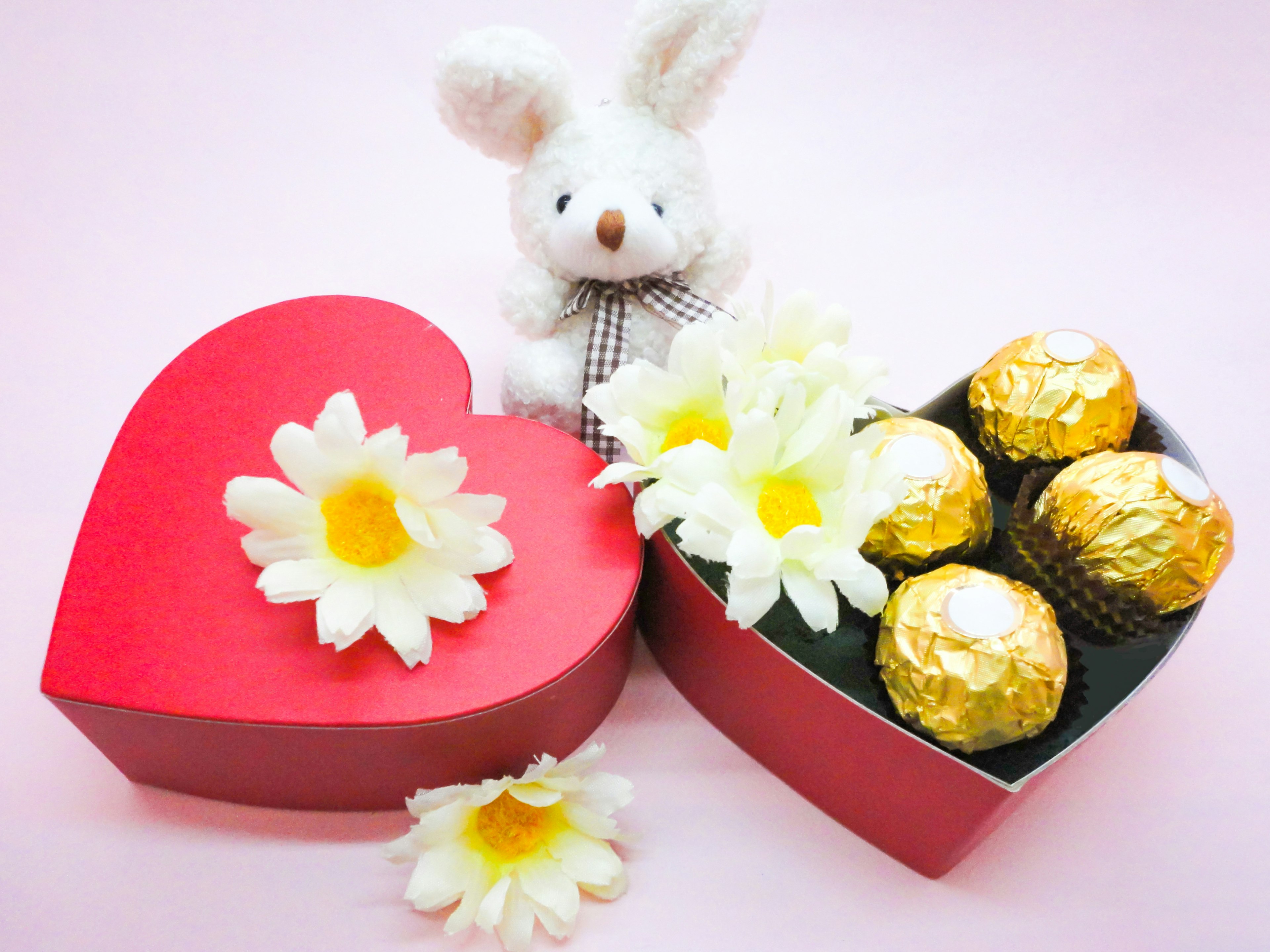 Un conejito de peluche junto a cajas en forma de corazón rojo y flores