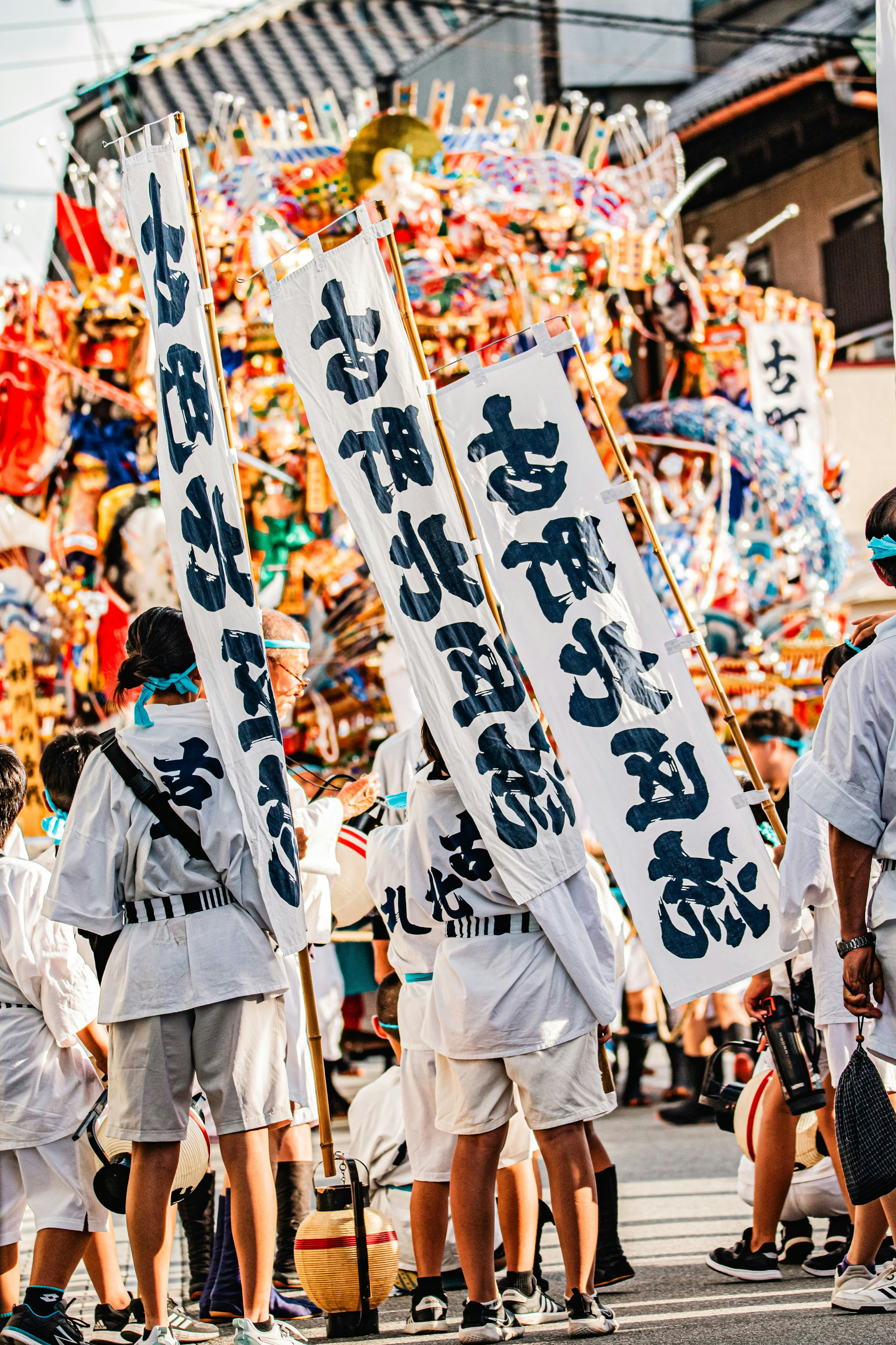 祭りの参加者が大きな飾りを持っている画像で白い衣装と大きな幕が特徴