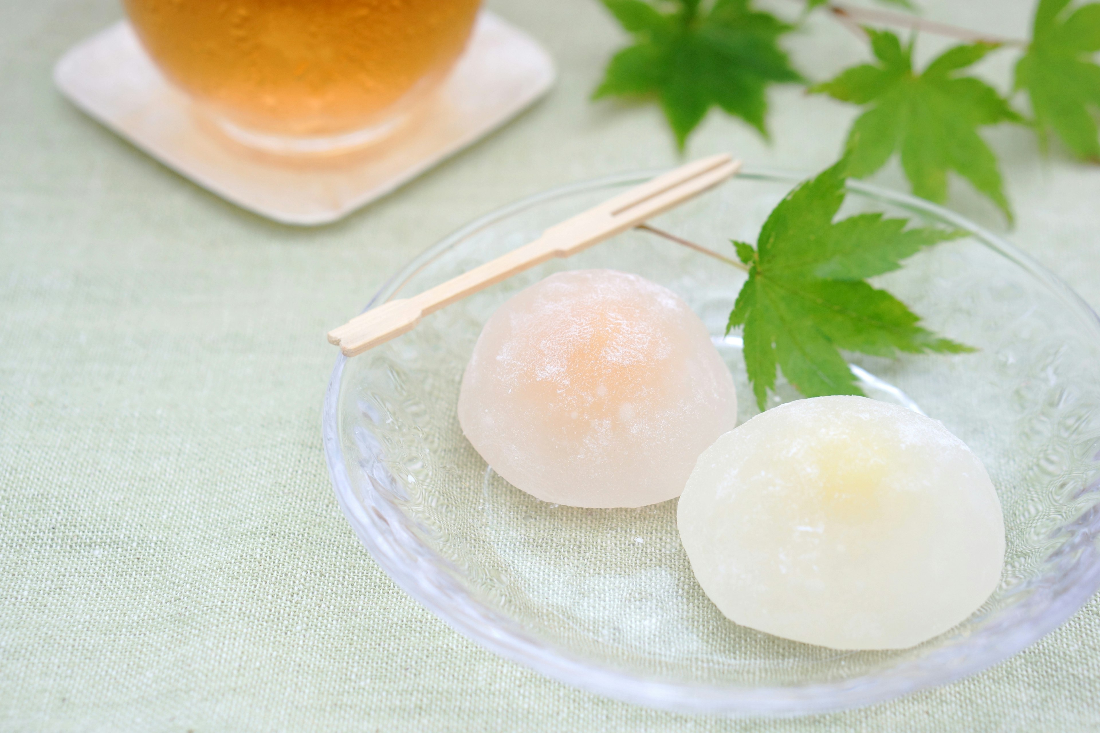 Zarte japanische Süßigkeiten auf einem Glasplatte mit grünen Blättern und Tee