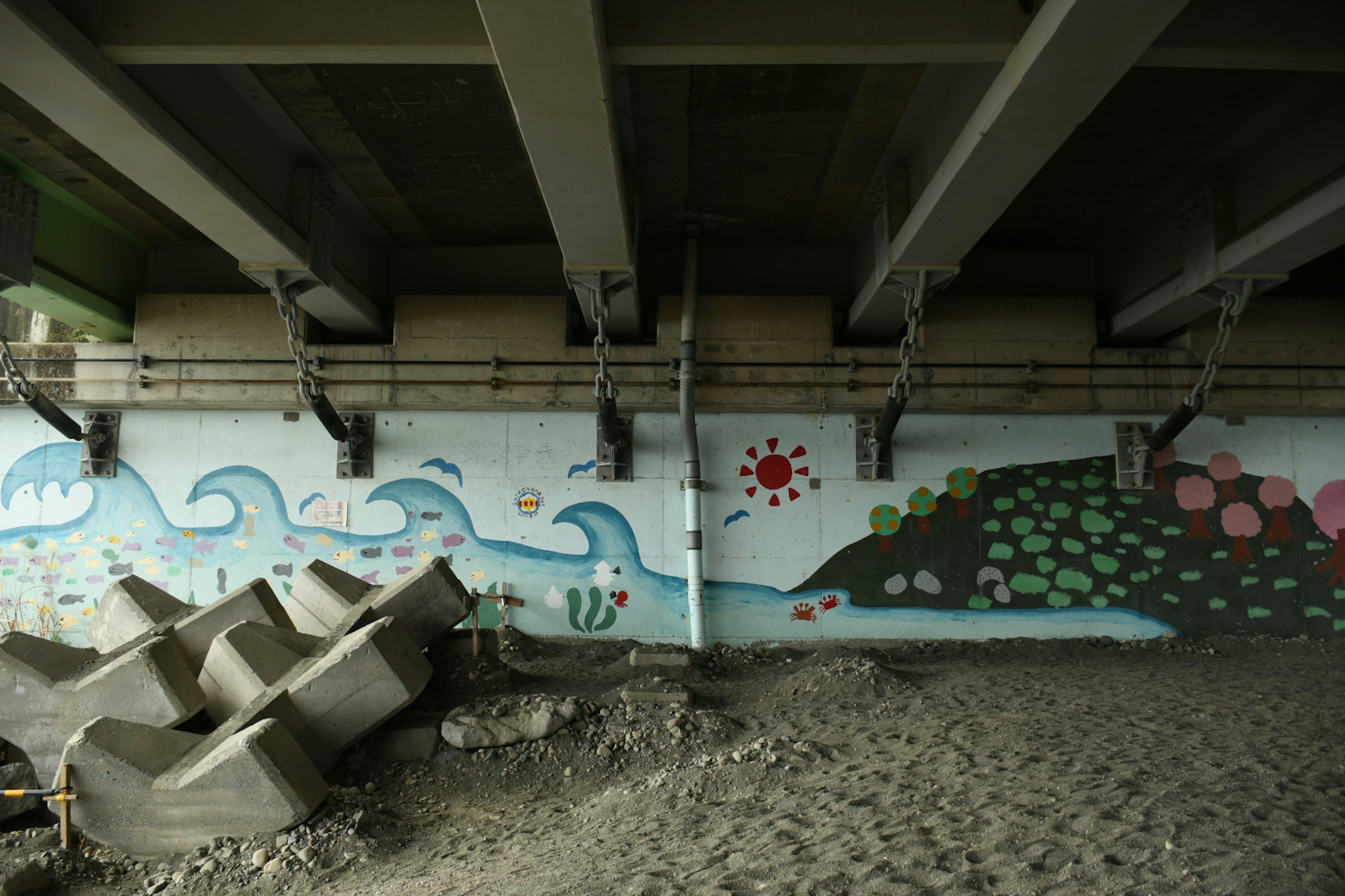 Mural berwarna di bawah jembatan menampilkan gelombang, gunung, dan desain matahari