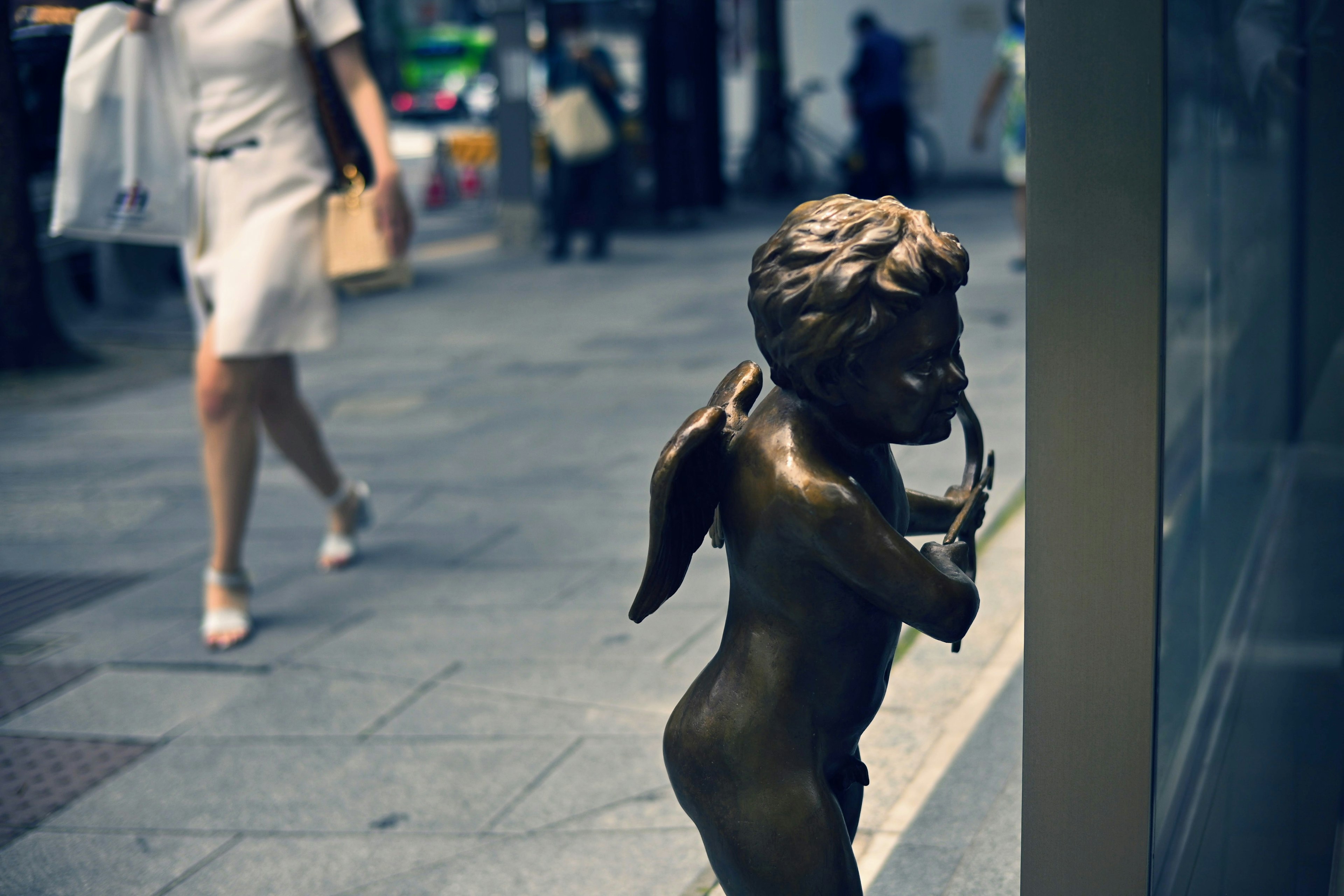 Bronze angel statue on the street with people walking