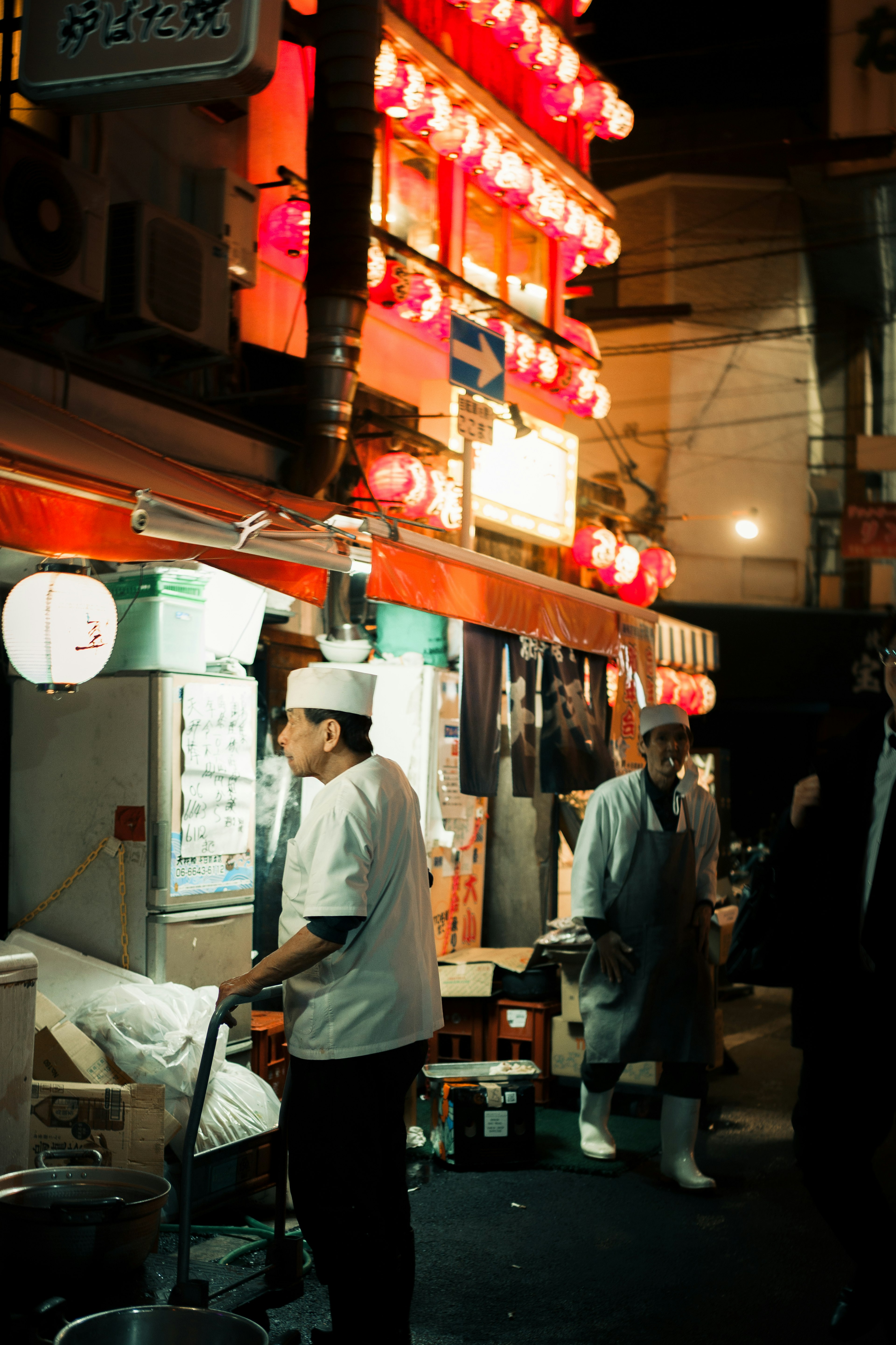 夜の屋台街で提灯が灯る中で働く料理人と通行人