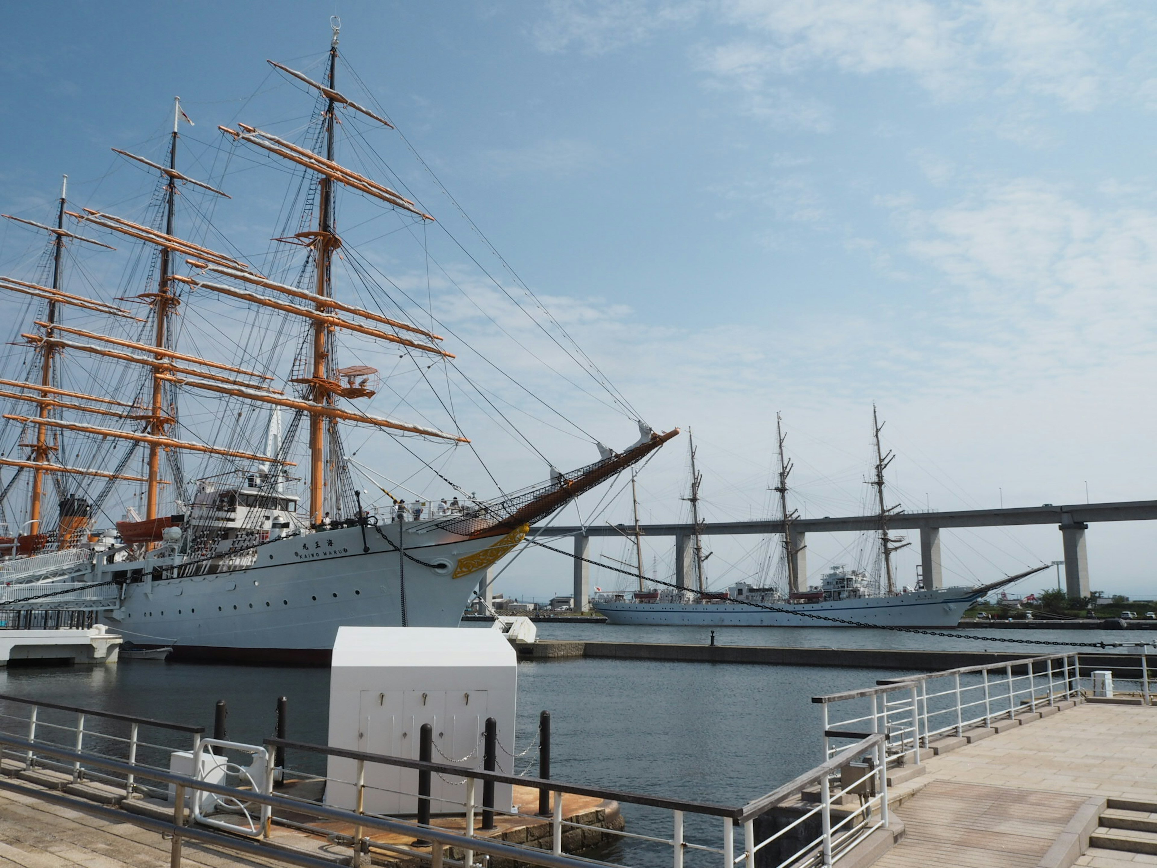 Large sailing ship docked under blue sky with nearby bridge