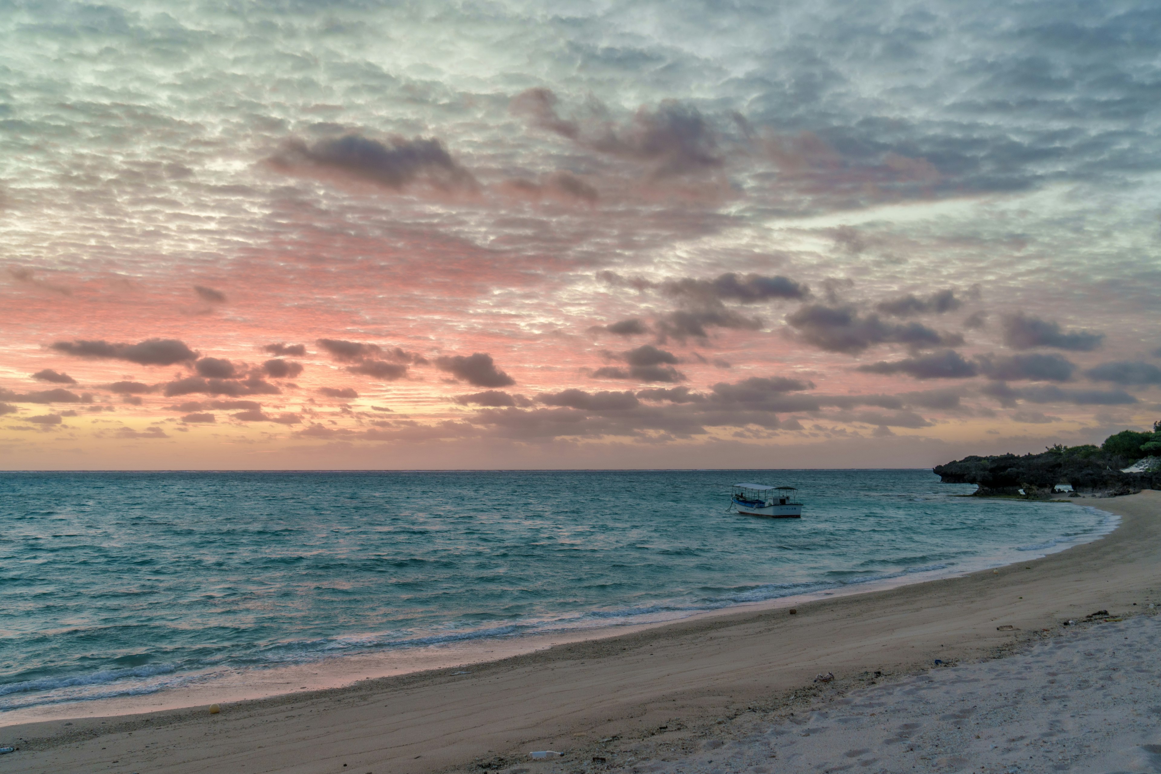 Beautiful beach scene at sunset with gentle waves and a boat visible