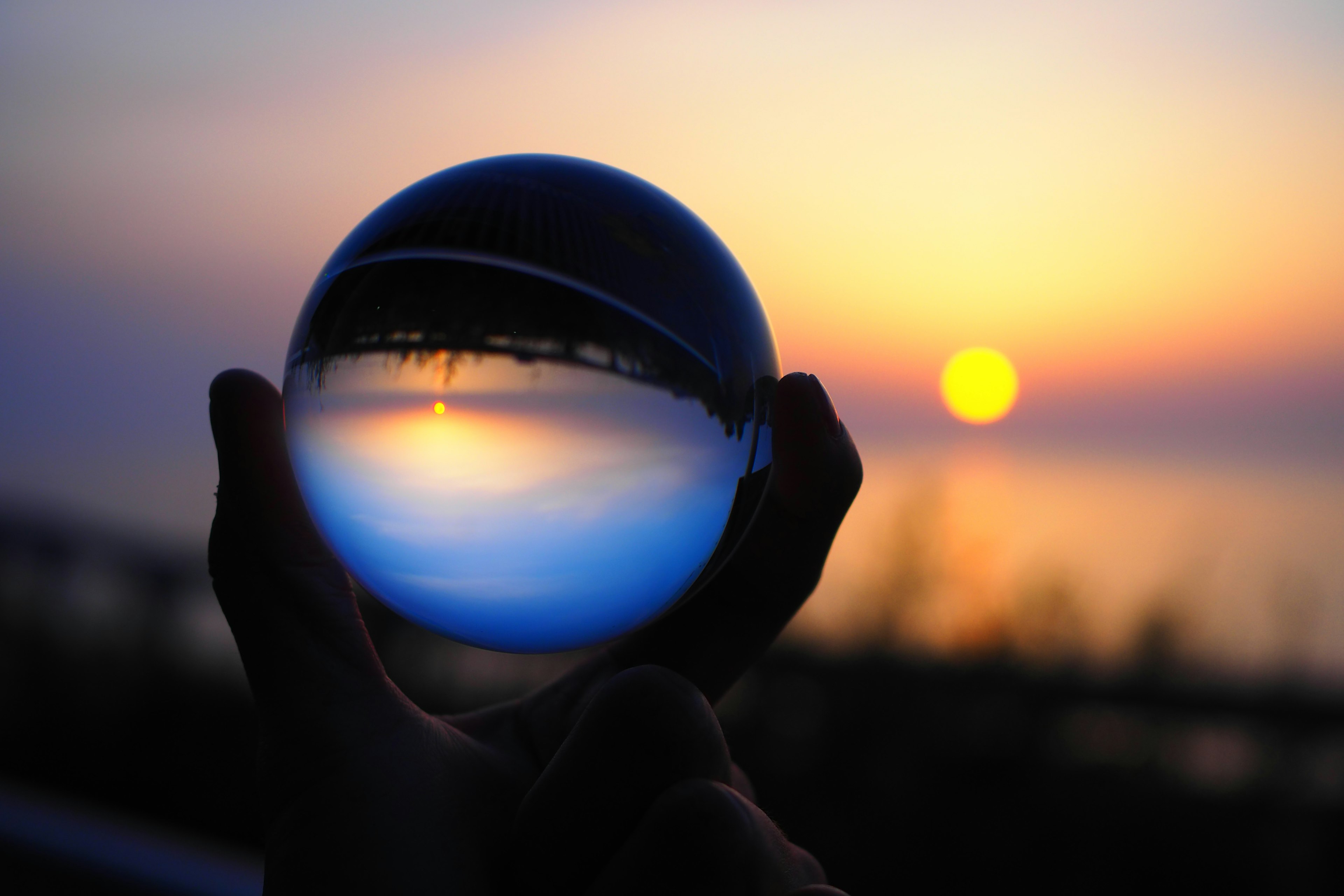 Hand holding a glass sphere reflecting a sunset