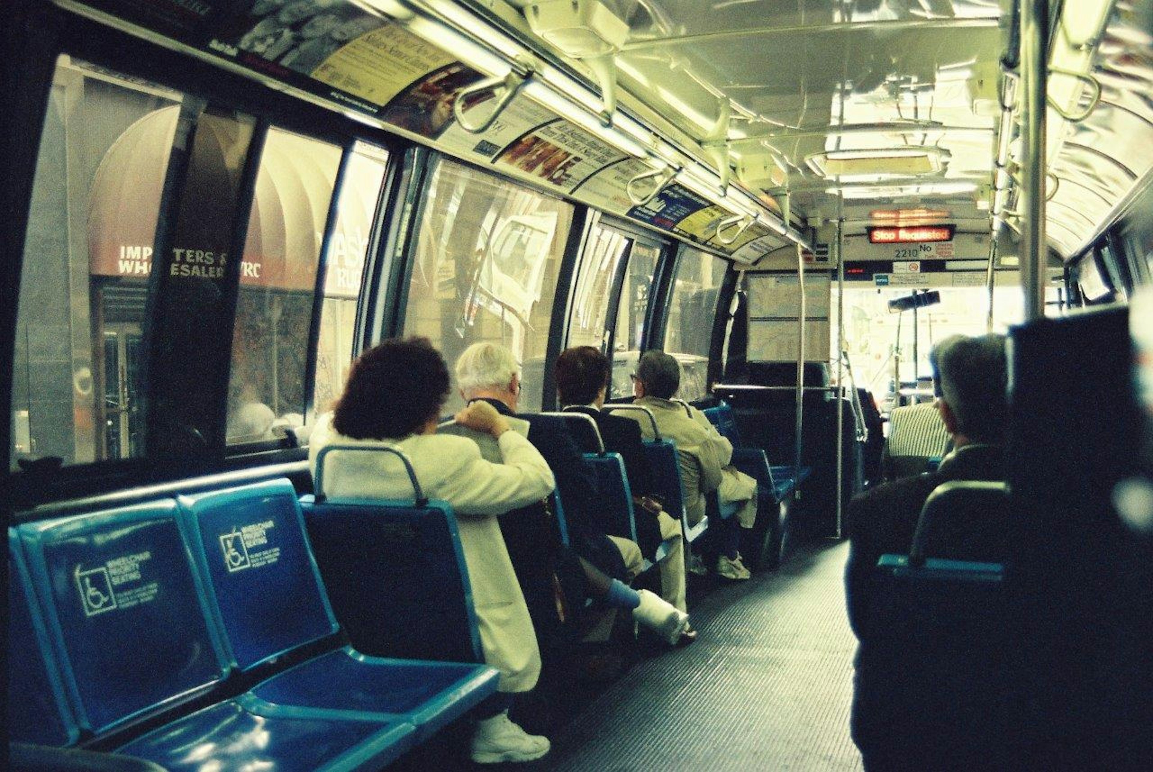 Interior of a bus with passengers seated on blue benches large windows visible