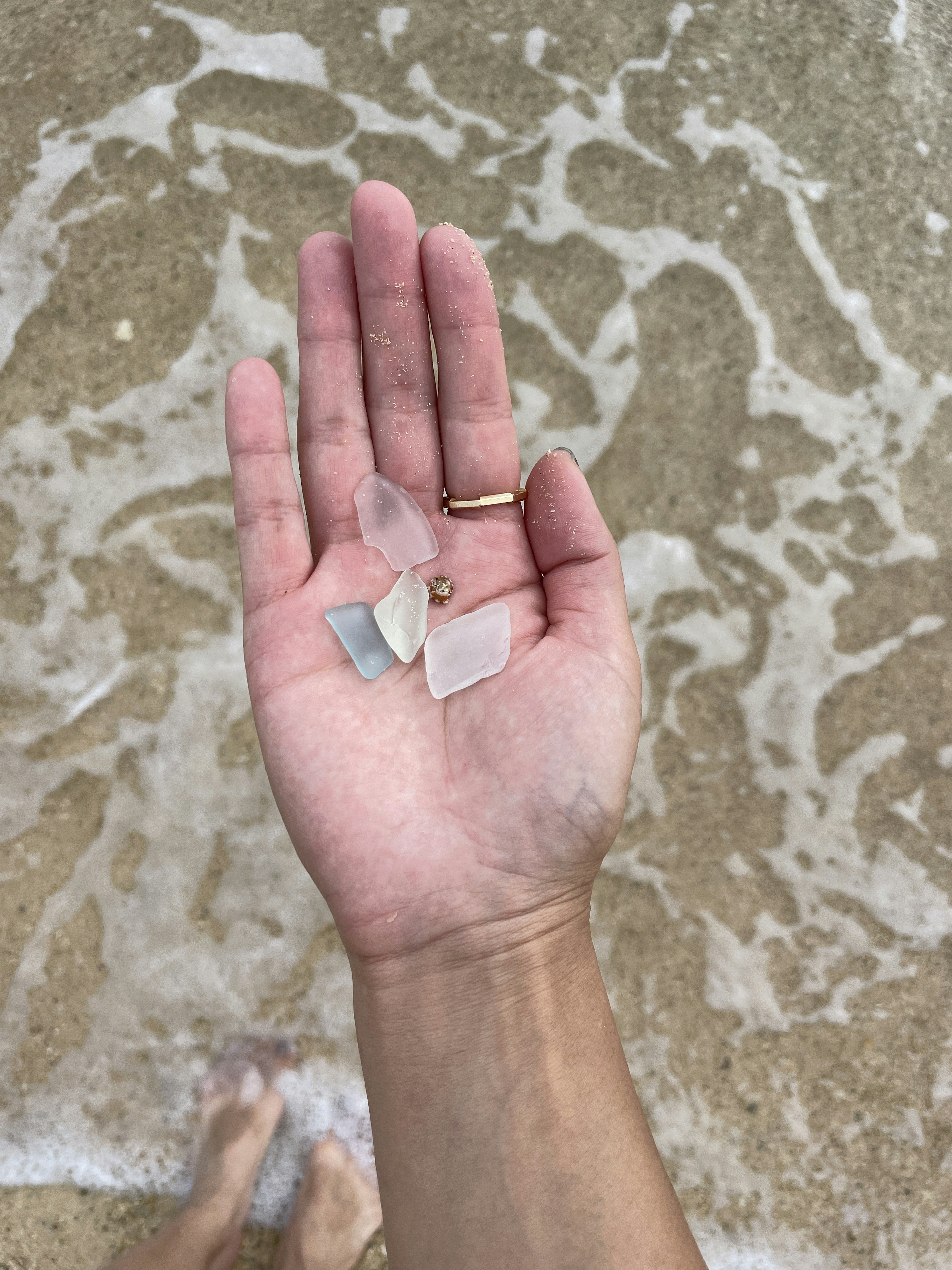 Mano che tiene pezzi di vetro di mare sopra una spiaggia sabbiosa