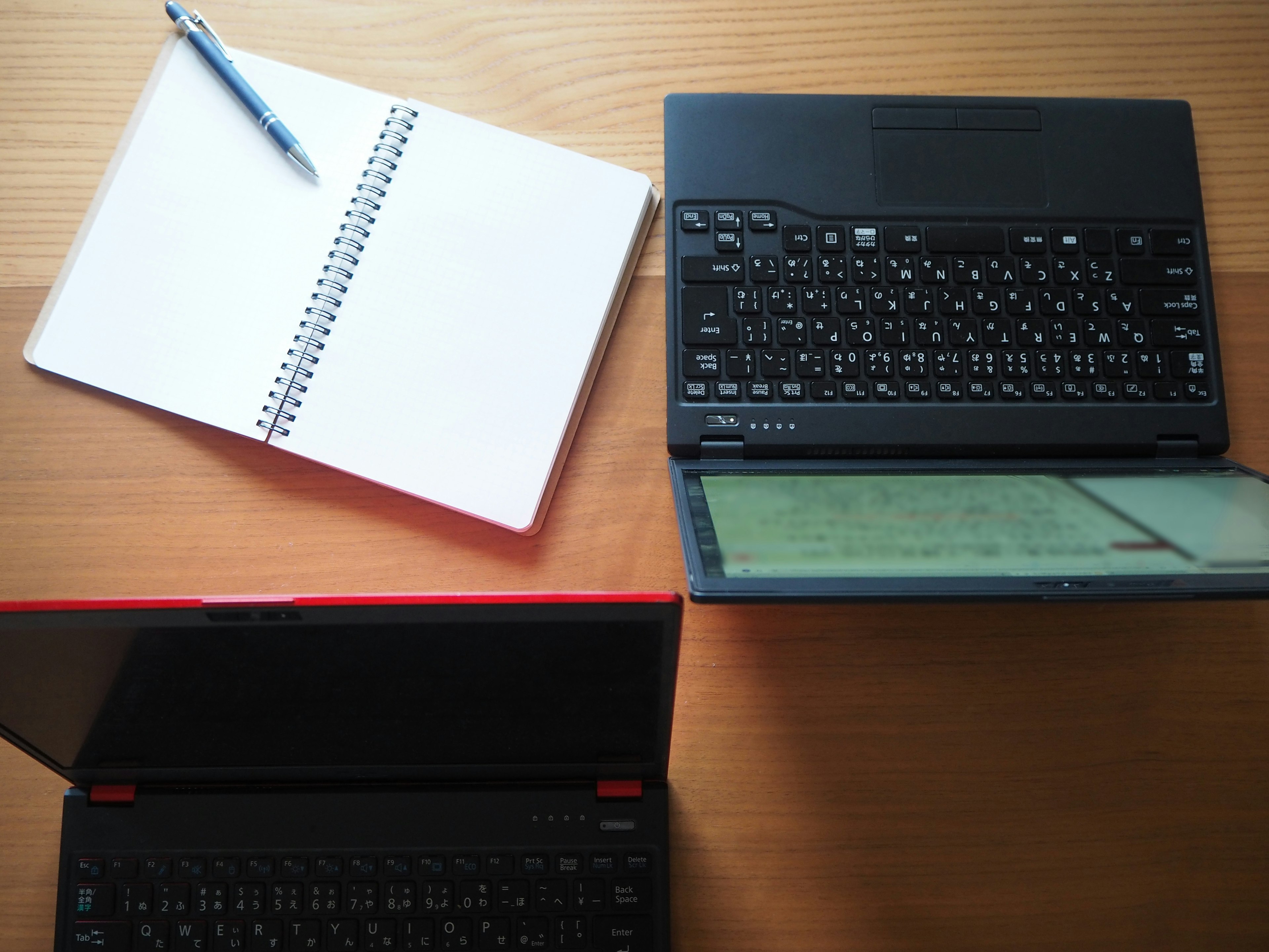 A quiet scene featuring laptops, a notebook, and a pen on a desk