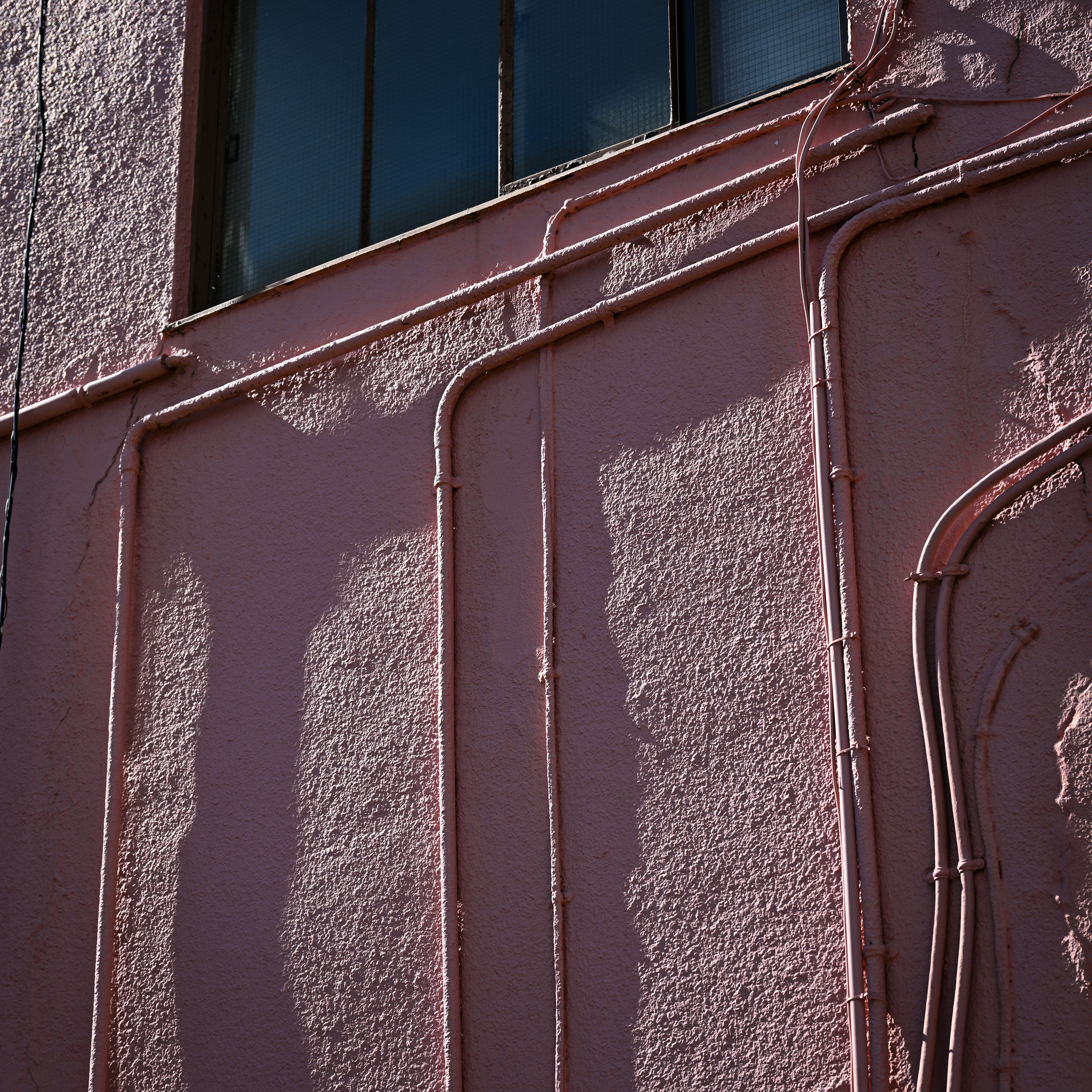 Pink wall with pipes casting shadows and a window