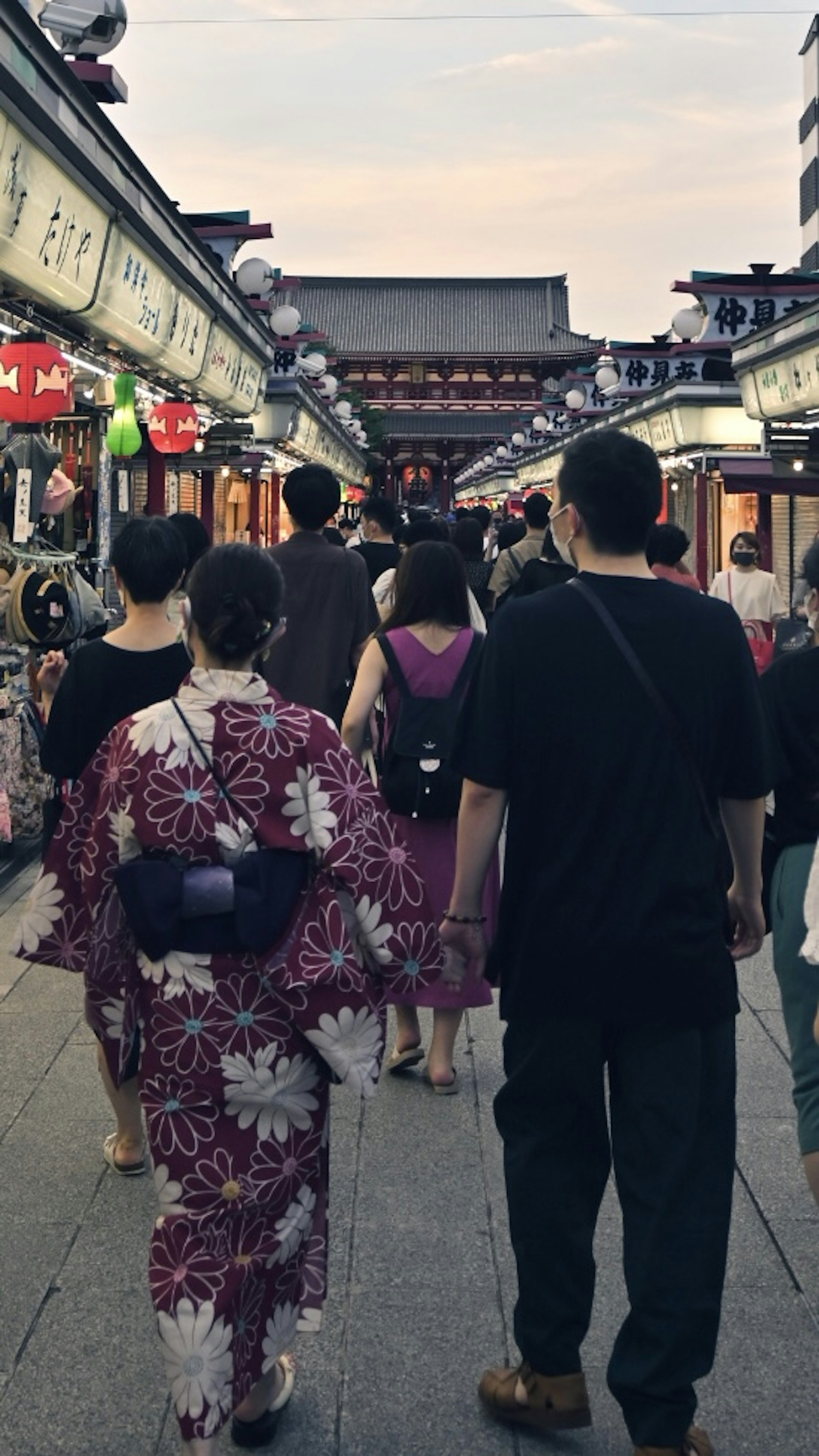 Personas caminando en una bulliciosa calle comercial al anochecer vistiendo yukata tradicionales