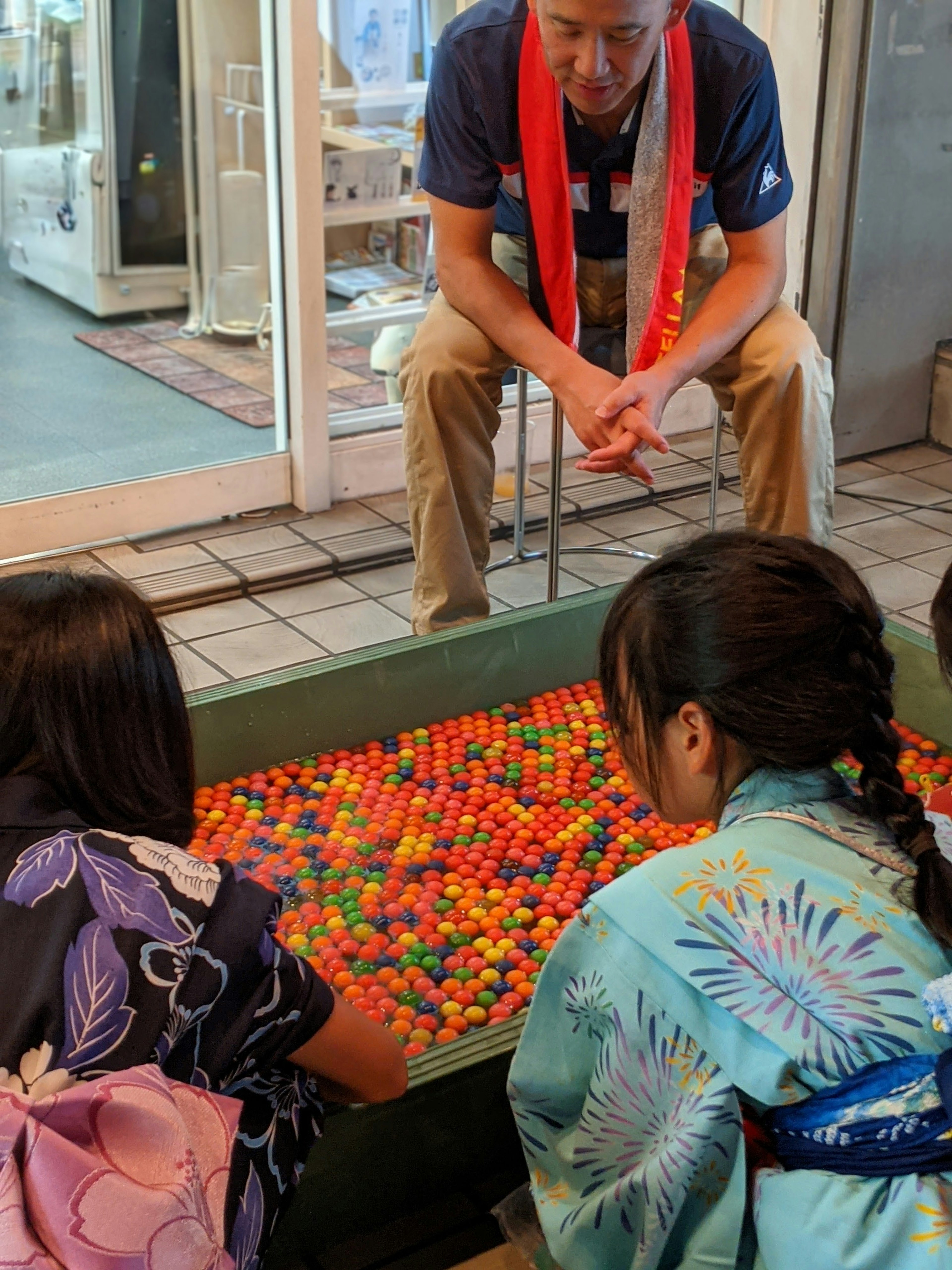 Kinder in Yukata spielen mit bunten Bällen, während ein Erwachsener zusieht