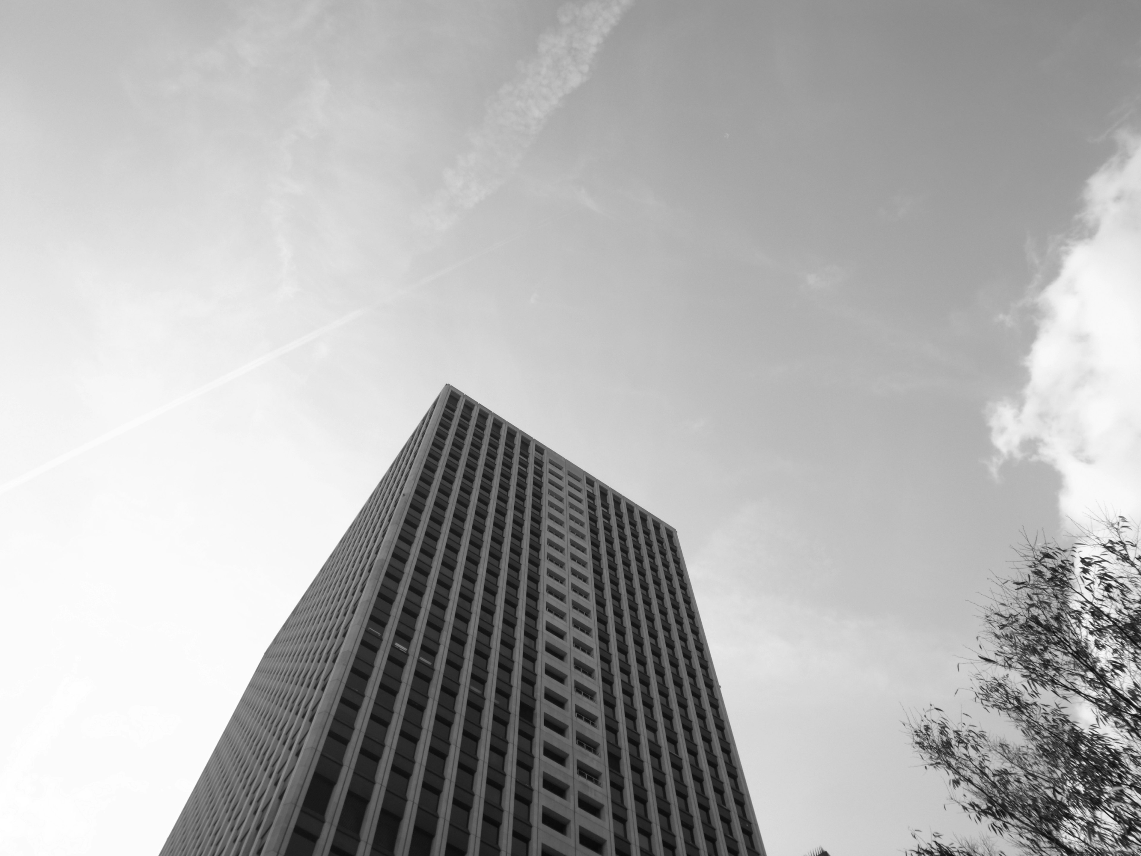 Photo en noir et blanc d'un gratte-ciel vu d'un angle bas Ciel clair avec des nuages visibles