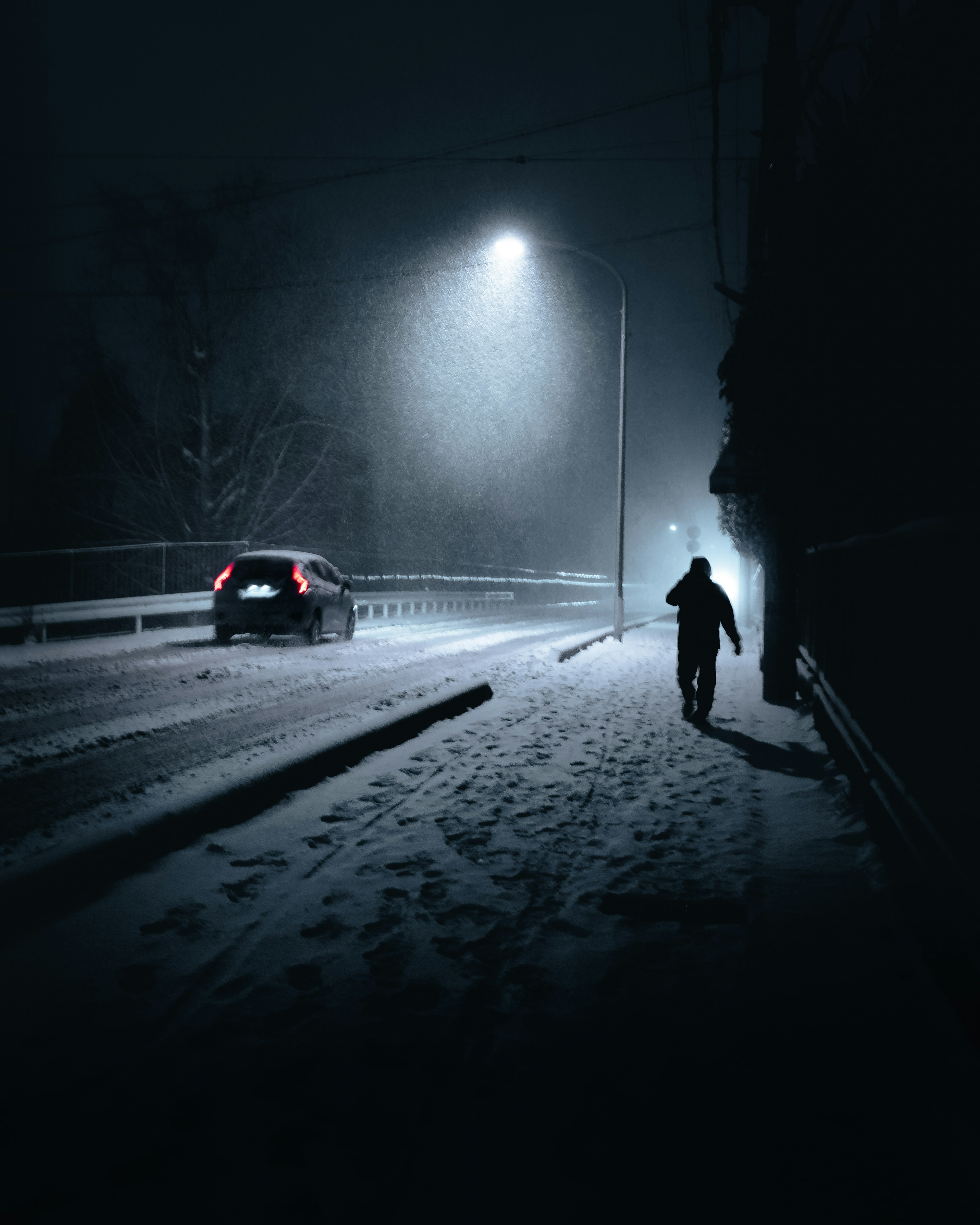 Una persona caminando en la nieve por la noche con un coche pasando