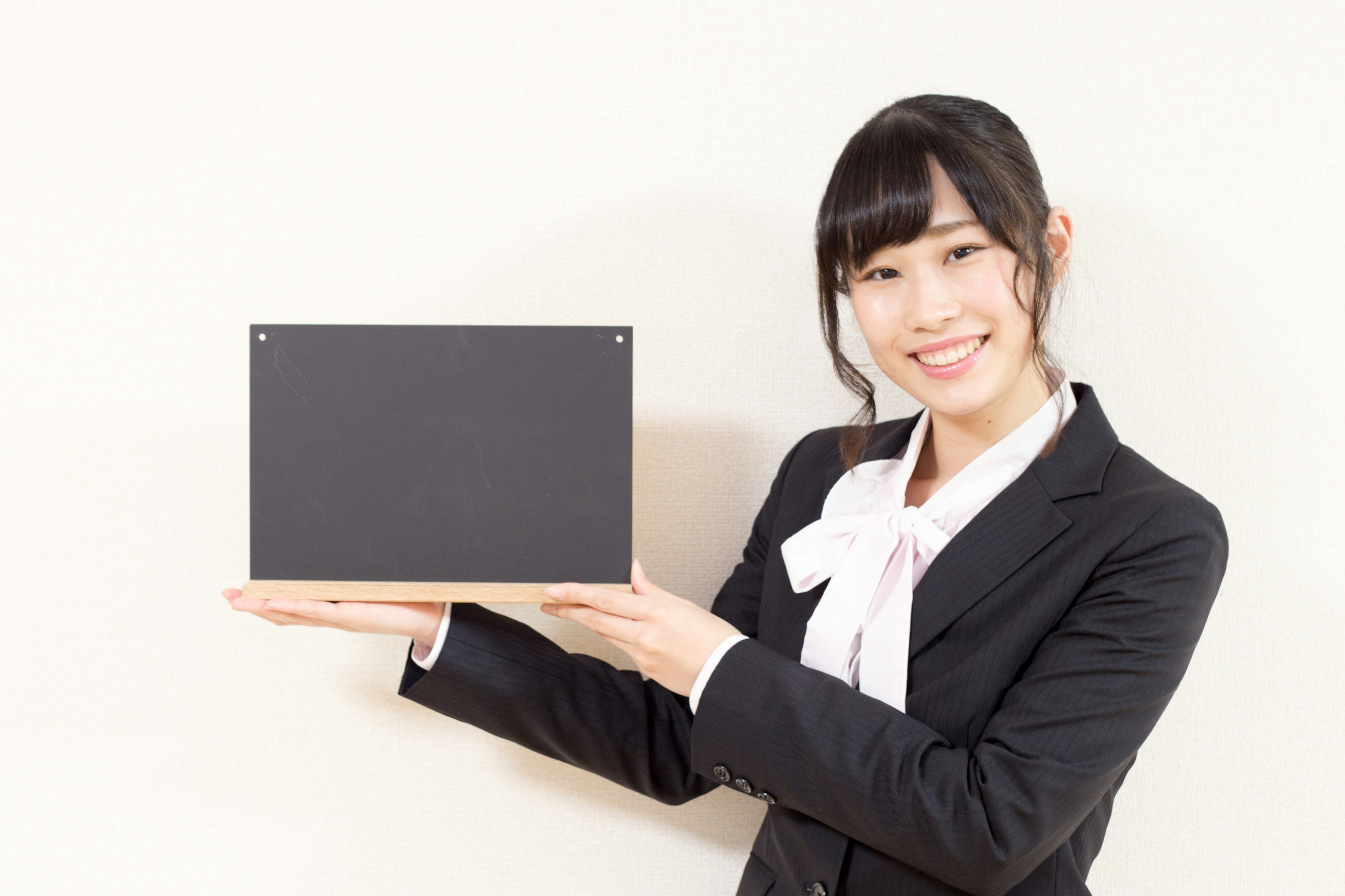 A woman in a business suit smiling while holding a black board