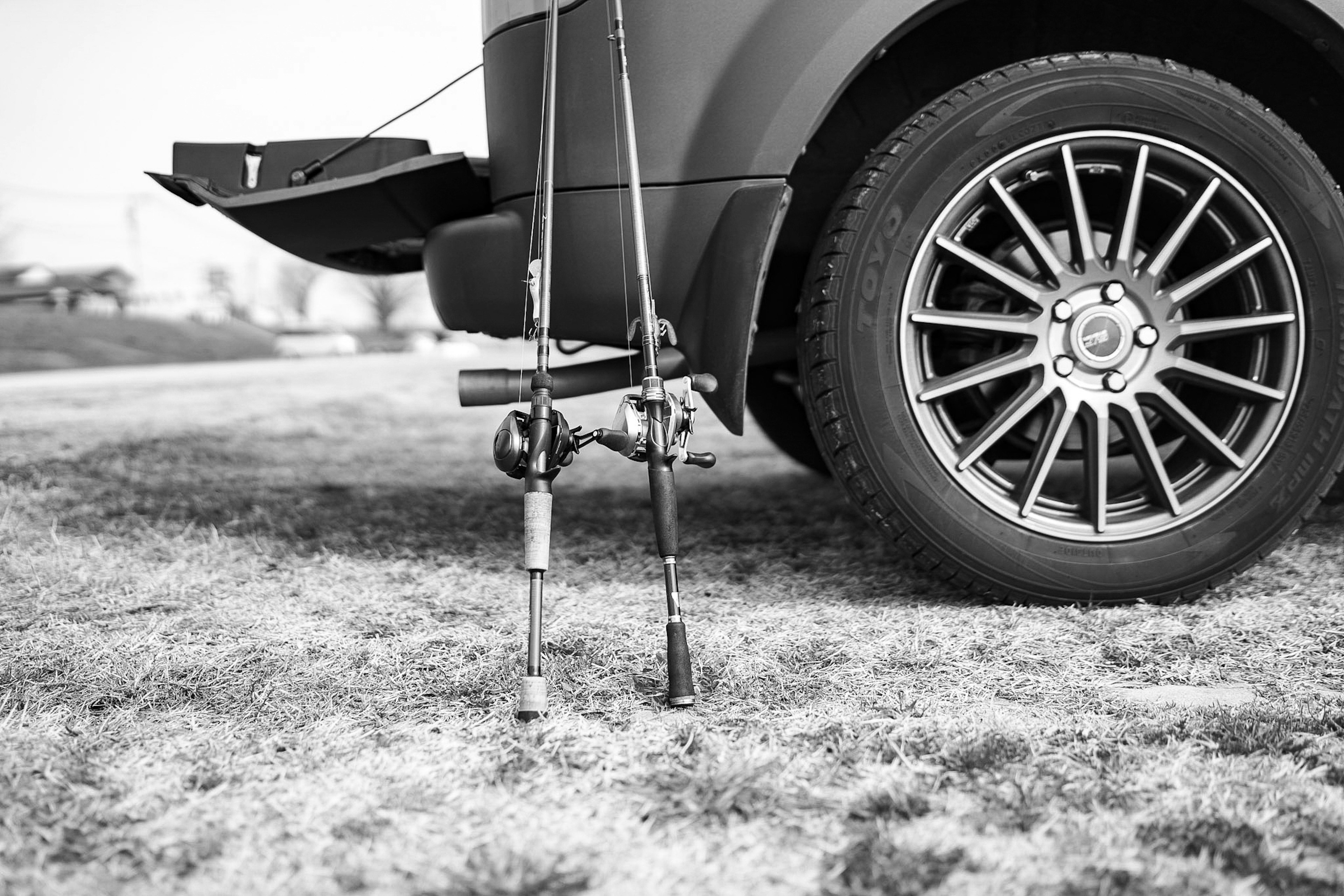 車のタイヤの横に立てかけられた釣り竿と草地