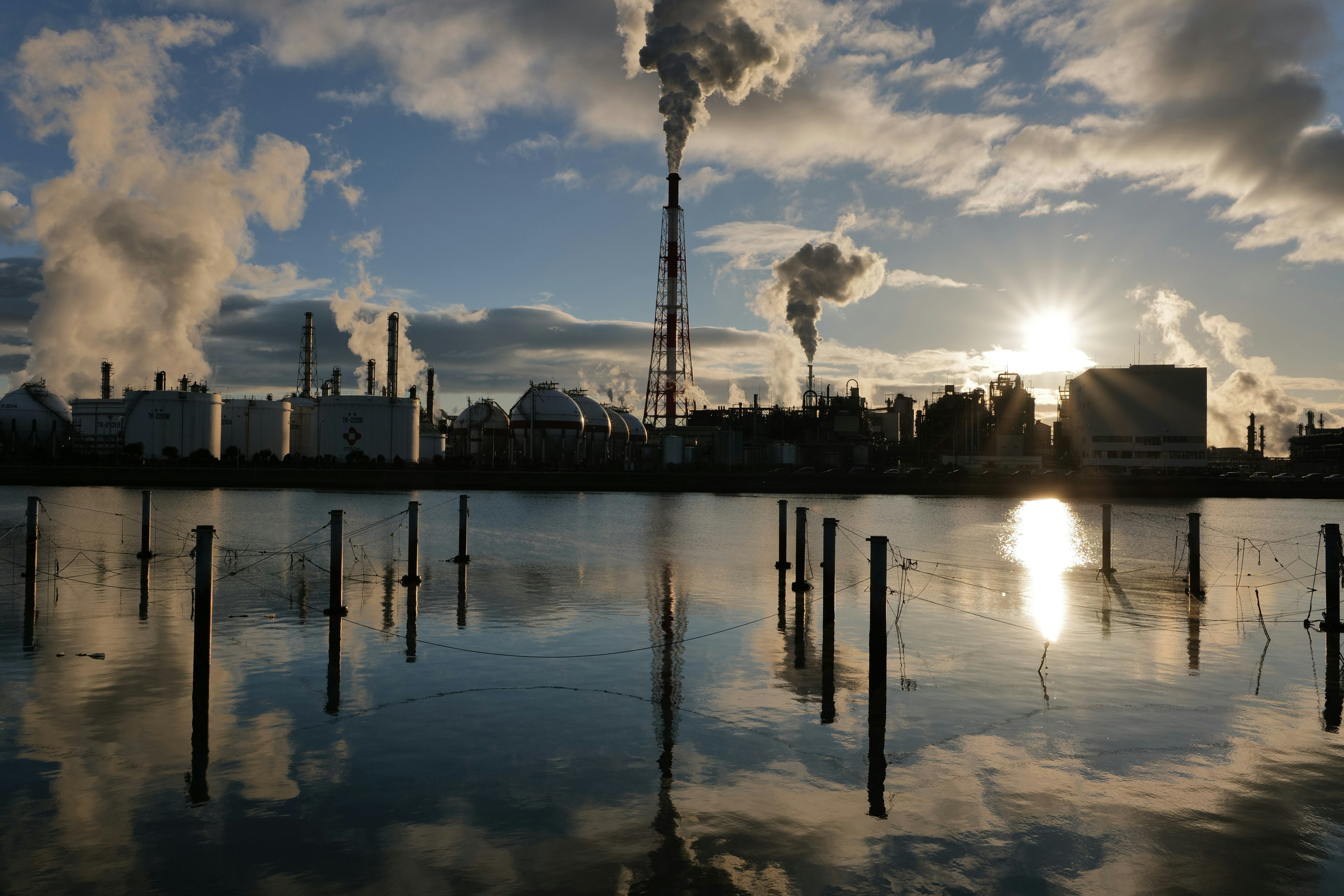 Industrial landscape with smoke rising from chimneys reflecting in the water at sunset